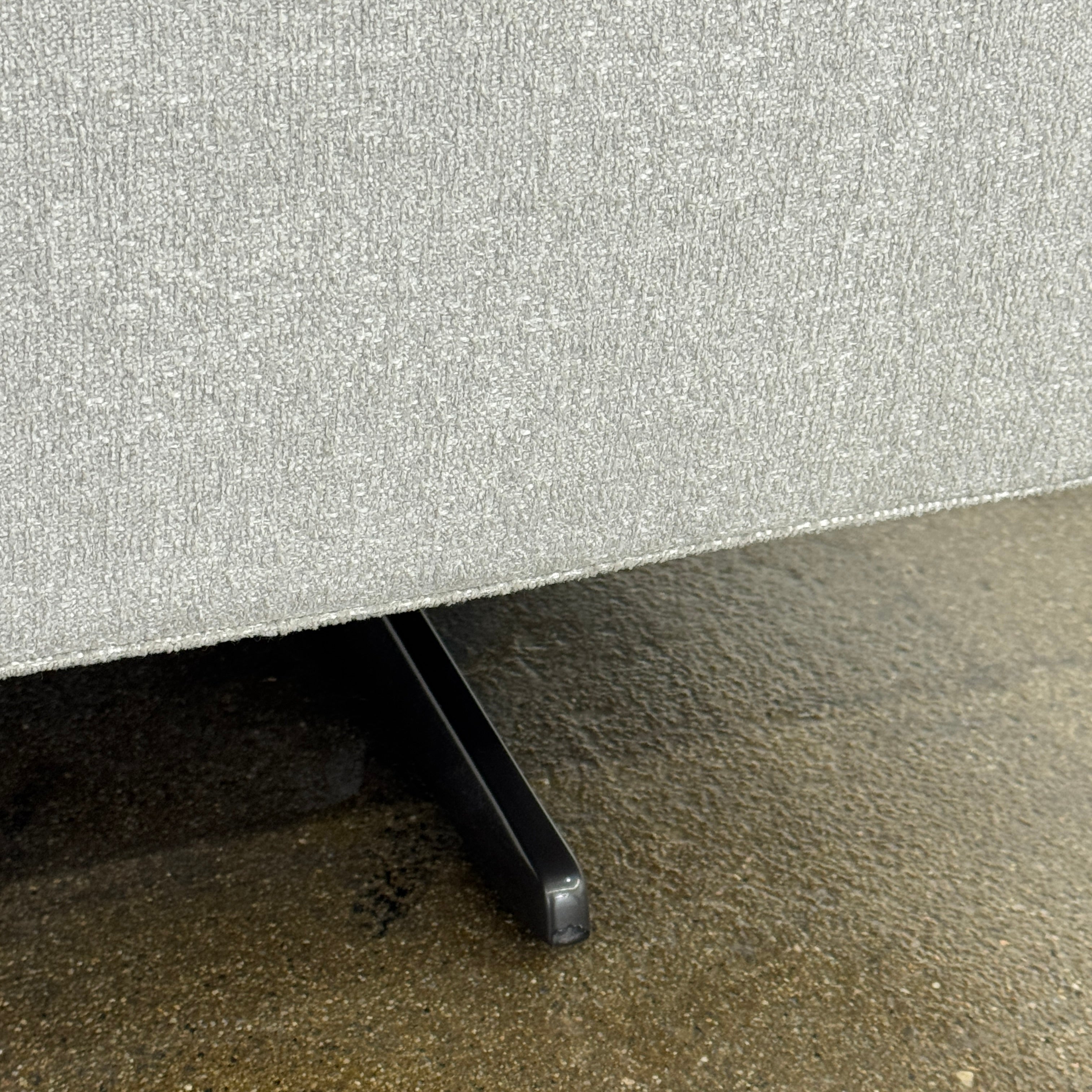 The Poliform Mondrian 2 piece Sectional Sofa with Headrests by Poliform, in light beige, features modern minimalist style with adjustable headrests and a black throw pillow, set on a concrete floor against a plain white wall.