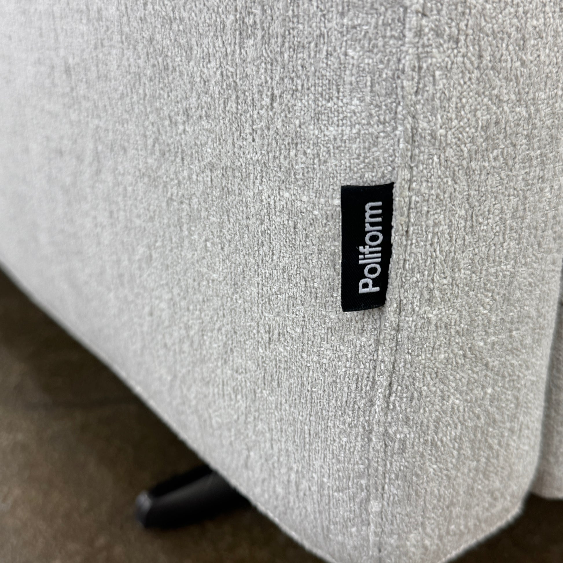 The Poliform Mondrian 2 piece Sectional Sofa with Headrests by Poliform, in light beige, features modern minimalist style with adjustable headrests and a black throw pillow, set on a concrete floor against a plain white wall.