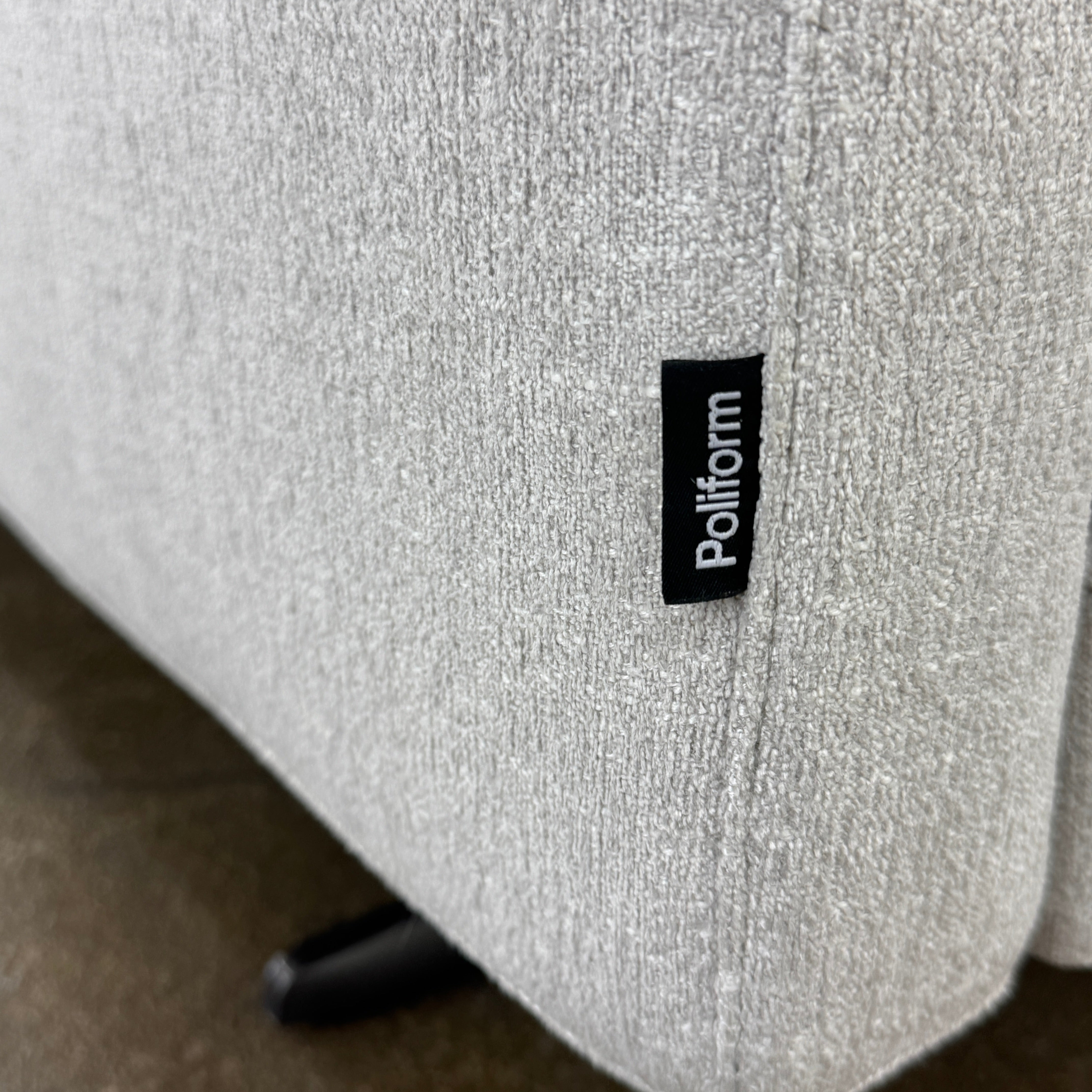 The Poliform Mondrian 2 piece Sectional Sofa with Headrests by Poliform, in light beige, features modern minimalist style with adjustable headrests and a black throw pillow, set on a concrete floor against a plain white wall.