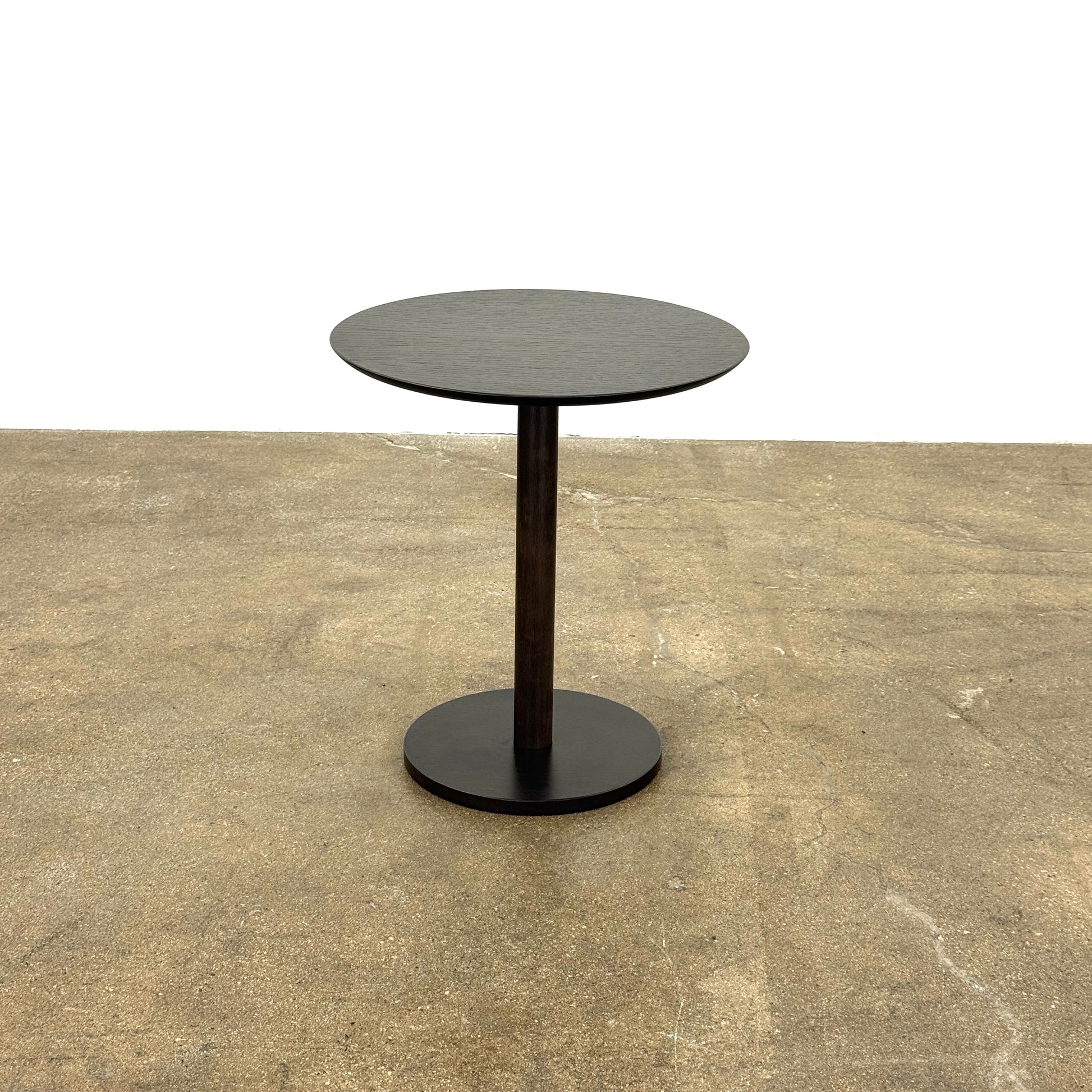 The Maruni Hiroshima Side Table by Maruni features a small, round black oak top and a single central pedestal base, shown against a plain light gray background.