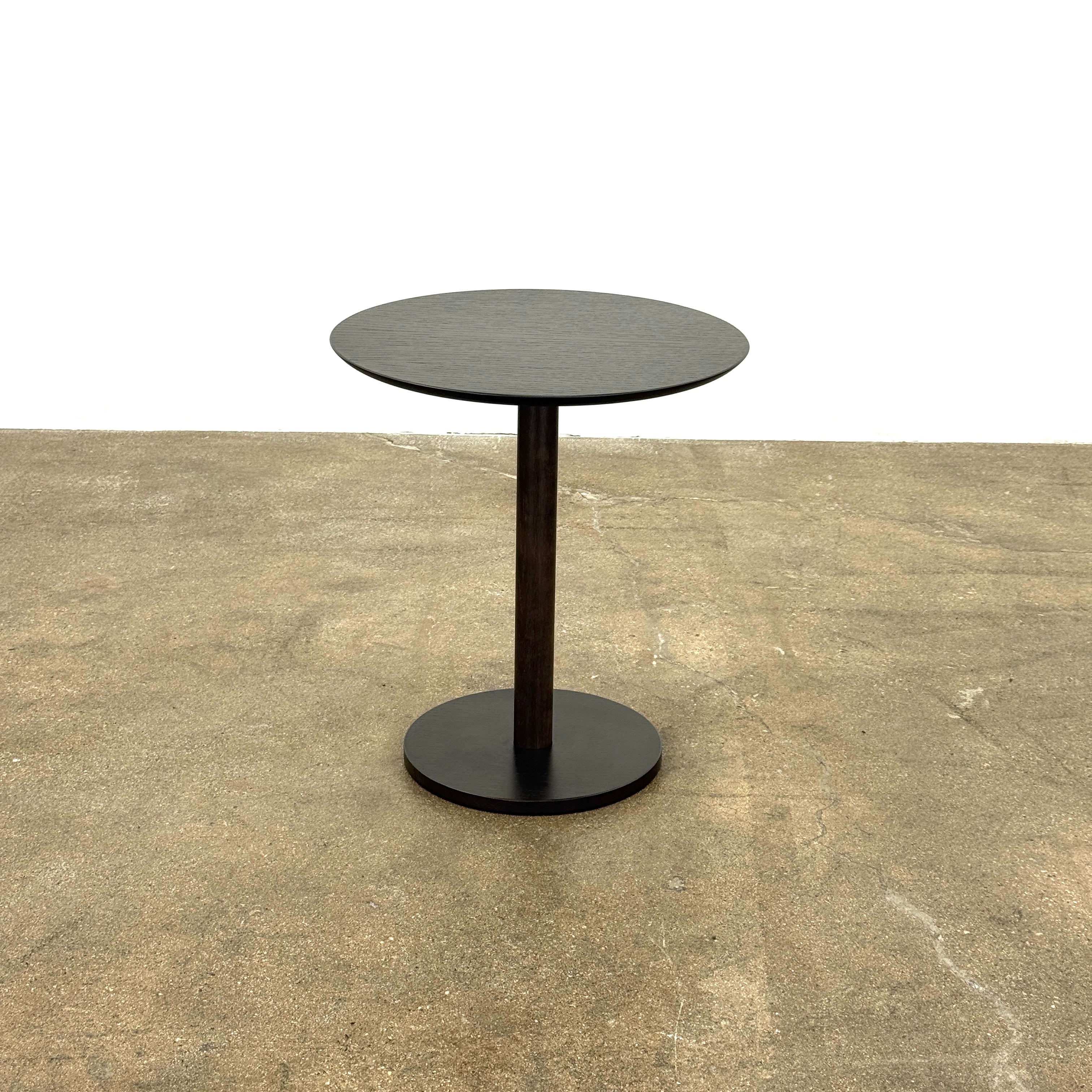 The Maruni Hiroshima Side Table by Maruni features a small, round black oak top and a single central pedestal base, shown against a plain light gray background.