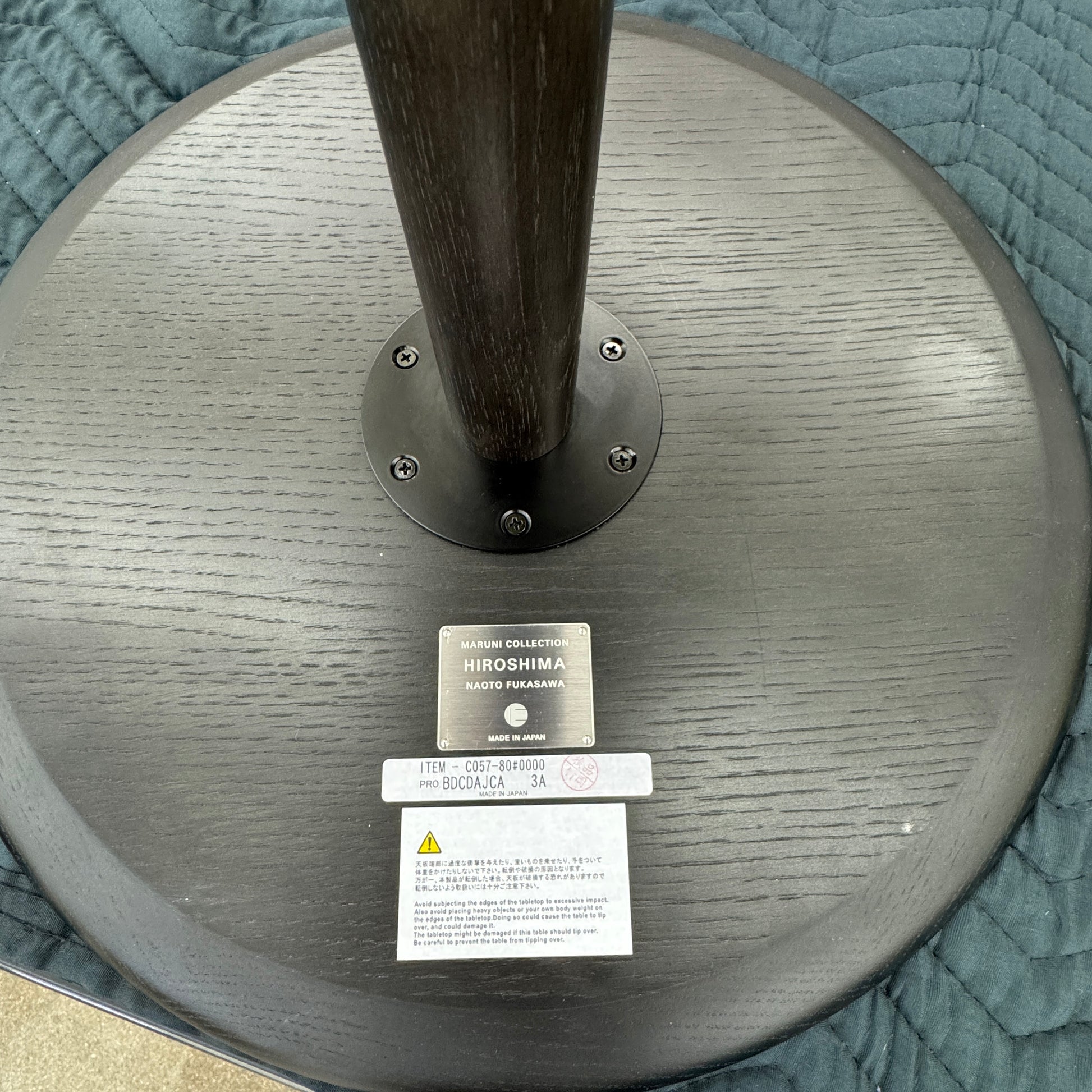 The Maruni Hiroshima Side Table by Maruni features a small, round black oak top and a single central pedestal base, shown against a plain light gray background.