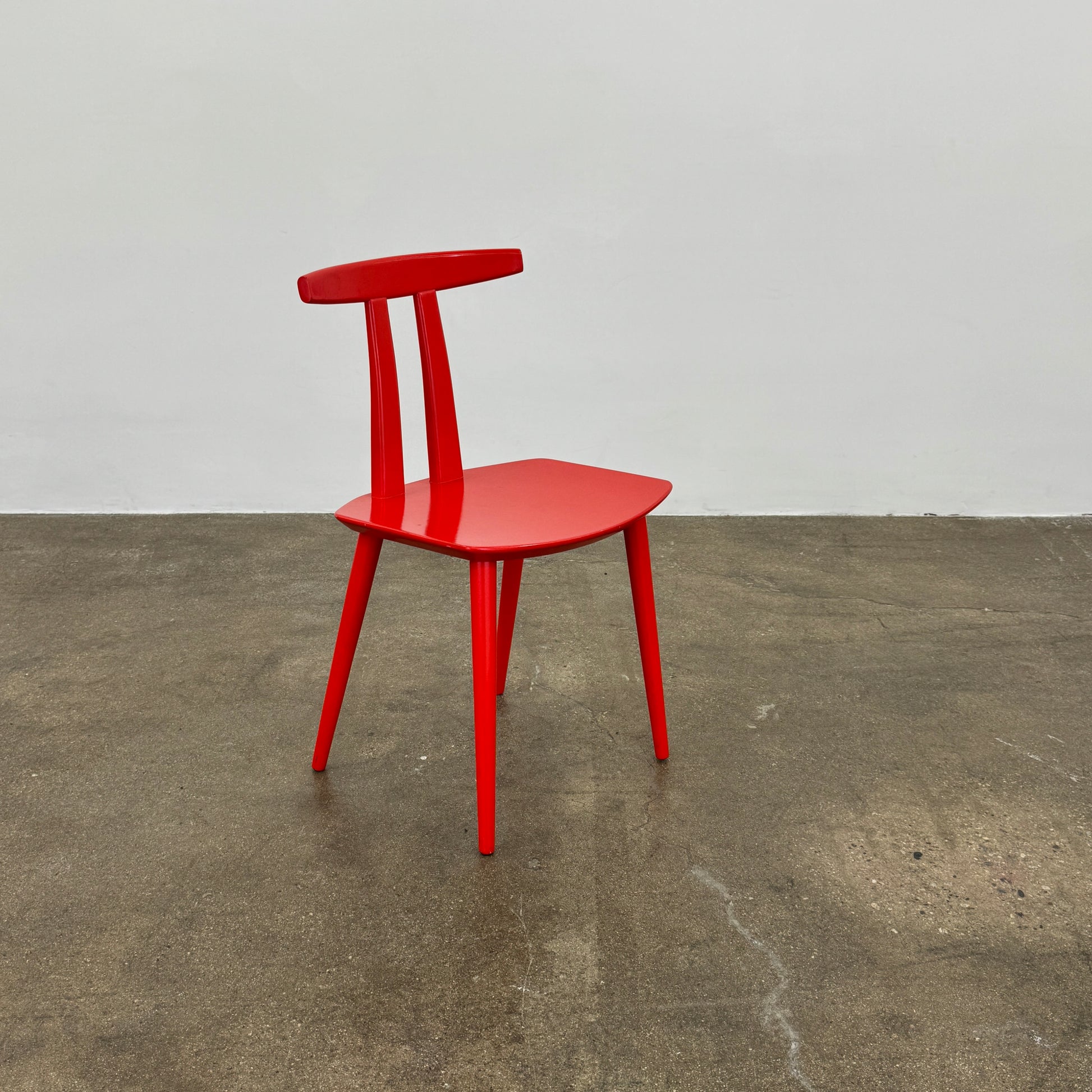 The Torii Chair by Bensen features a minimalist design with a round backrest and angled legs, crafted in red wood. Shown against a plain light background, this piece showcases Bensen's signature style.