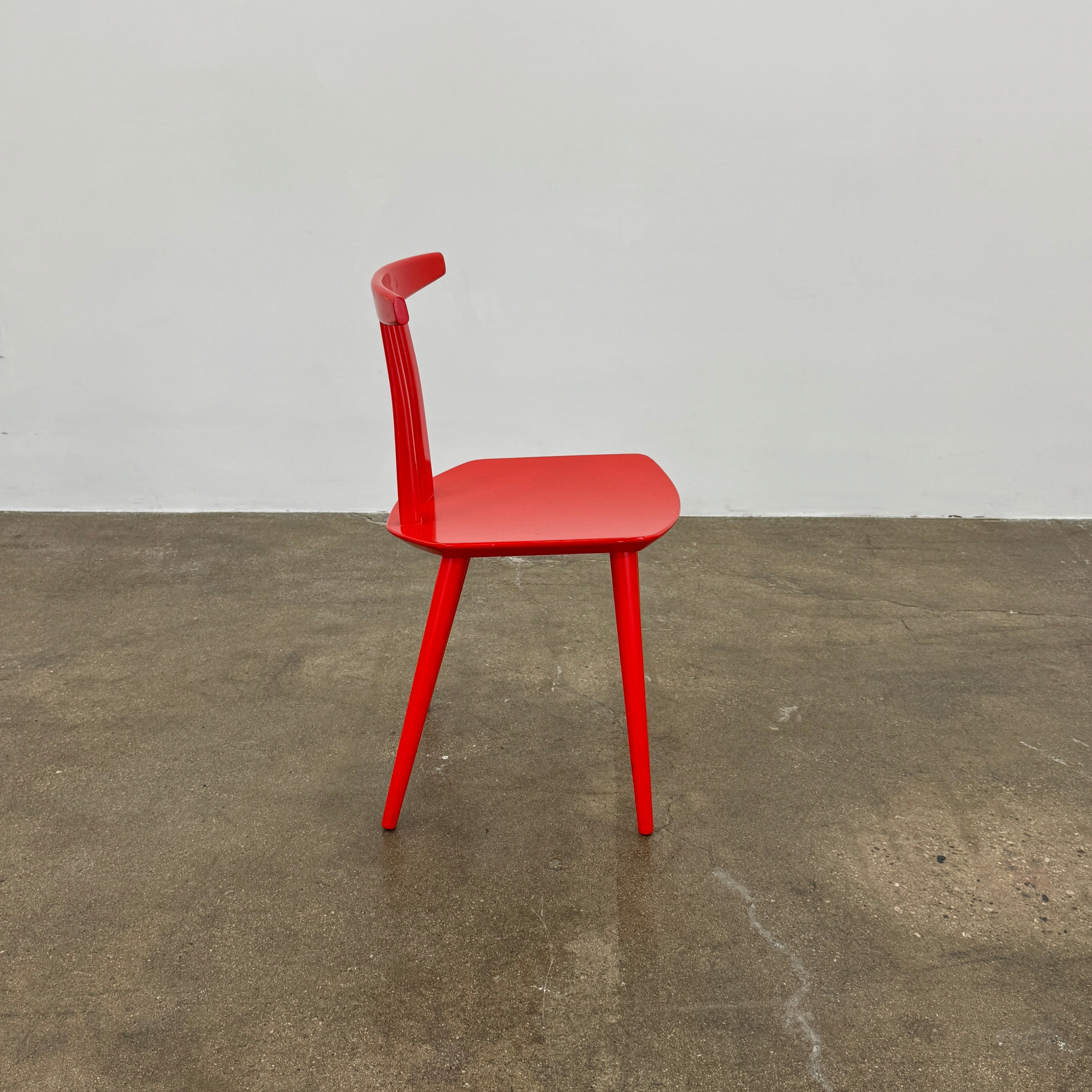 The Torii Chair by Bensen features a minimalist design with a round backrest and angled legs, crafted in red wood. Shown against a plain light background, this piece showcases Bensen's signature style.