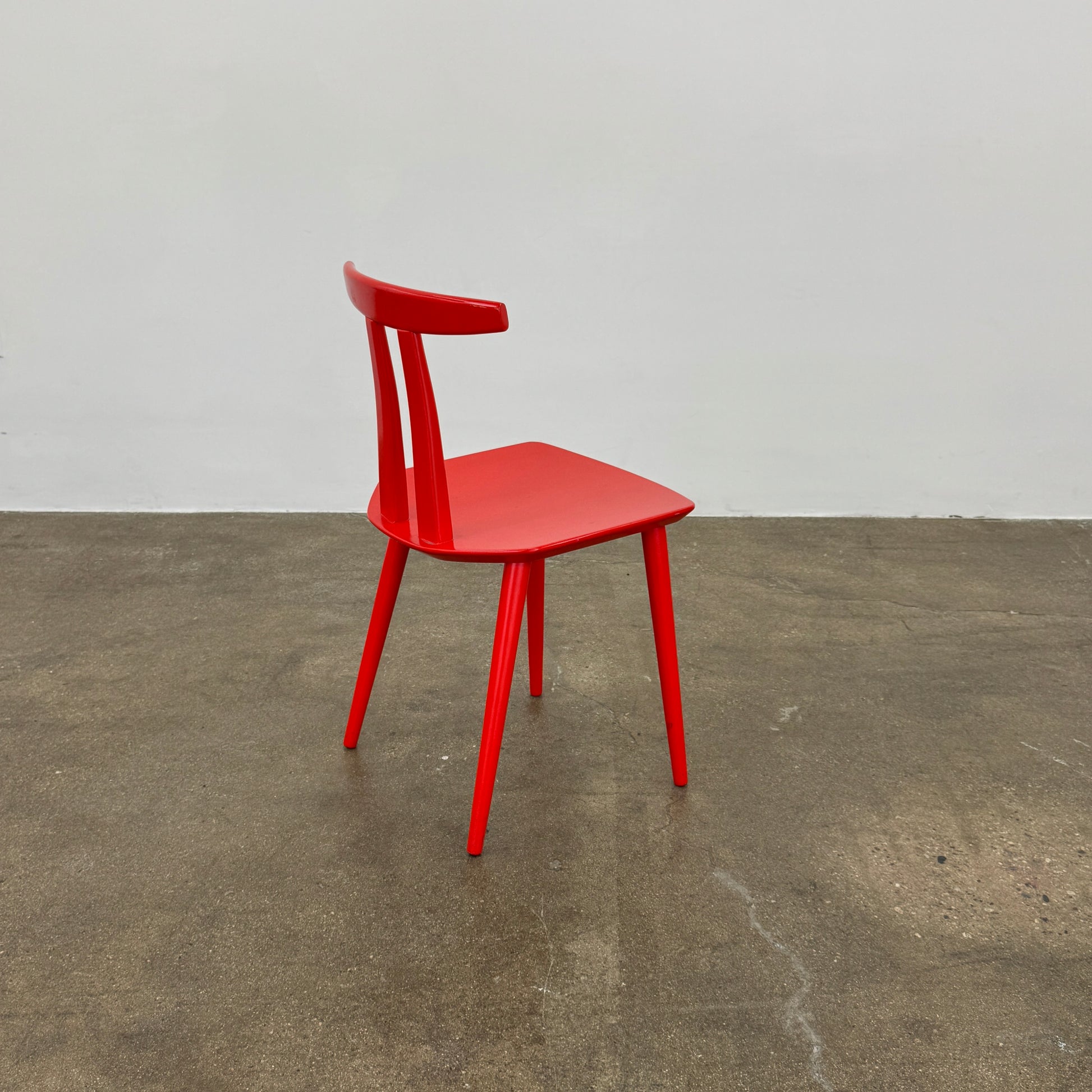 The Torii Chair by Bensen features a minimalist design with a round backrest and angled legs, crafted in red wood. Shown against a plain light background, this piece showcases Bensen's signature style.