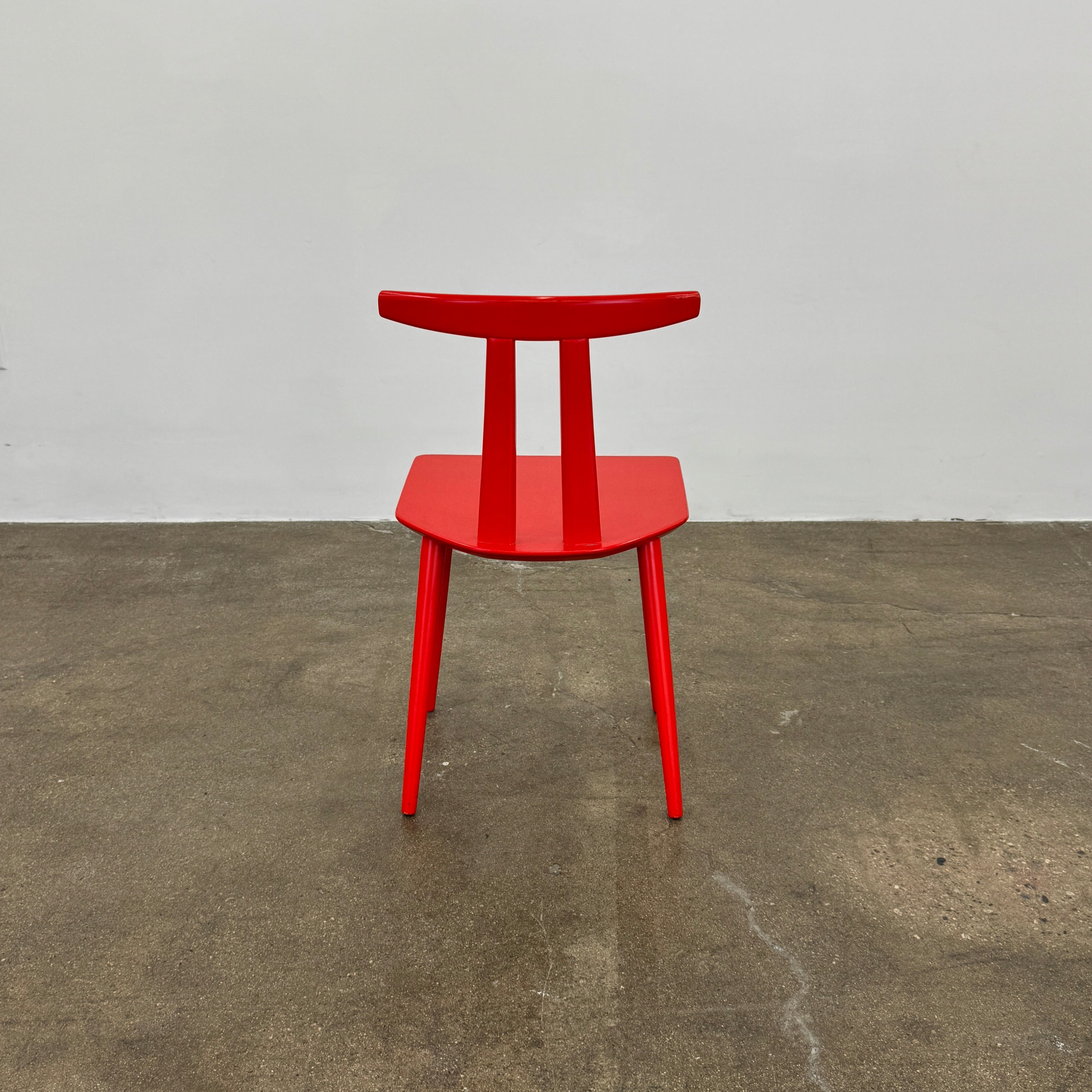 The Torii Chair by Bensen features a minimalist design with a round backrest and angled legs, crafted in red wood. Shown against a plain light background, this piece showcases Bensen's signature style.