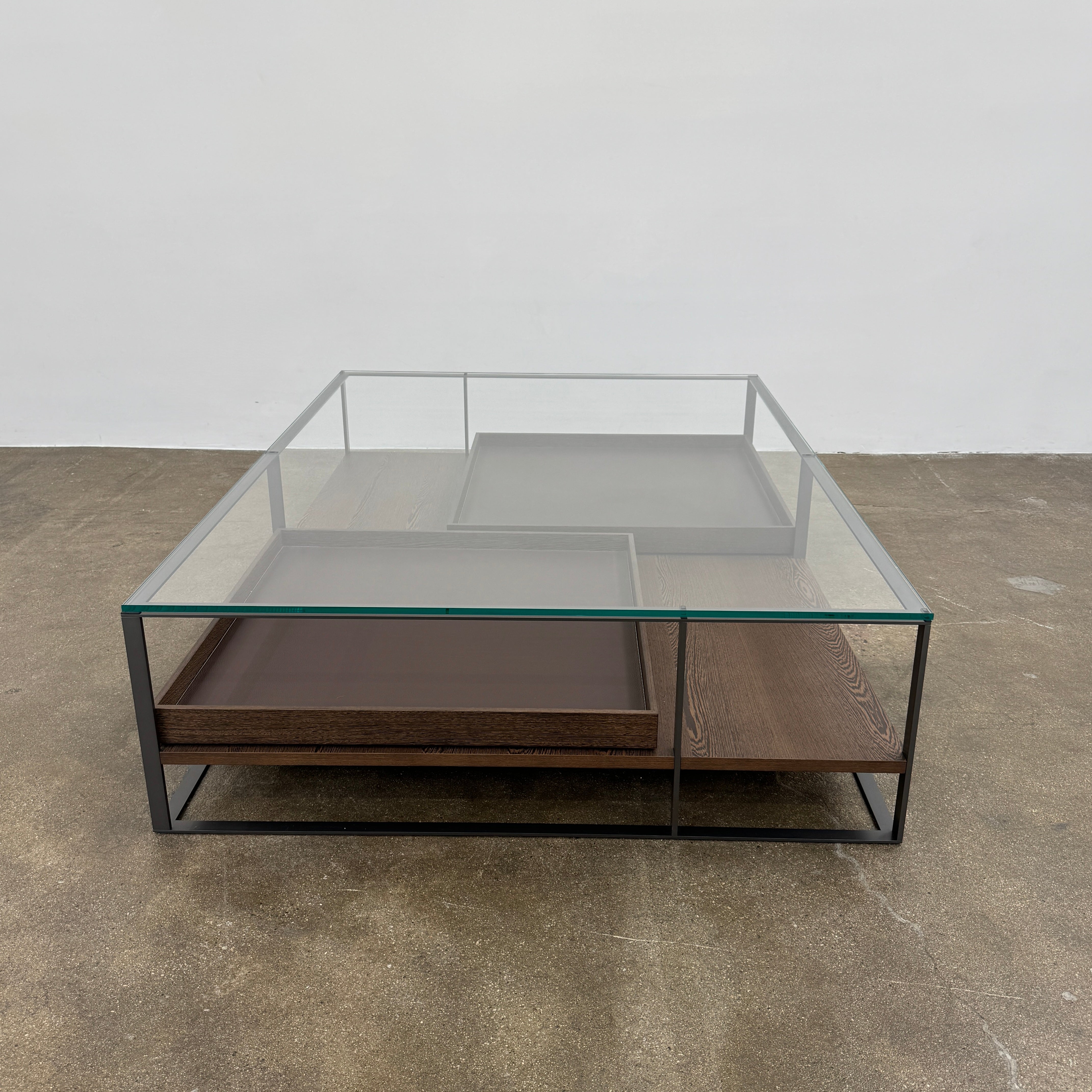 The Maxalto Lithos Coffee Table by Maxalto features a square metal frame, glass top, and two wooden lower shelves—one slightly raised—inspired by the original design. Shown against a plain white background.