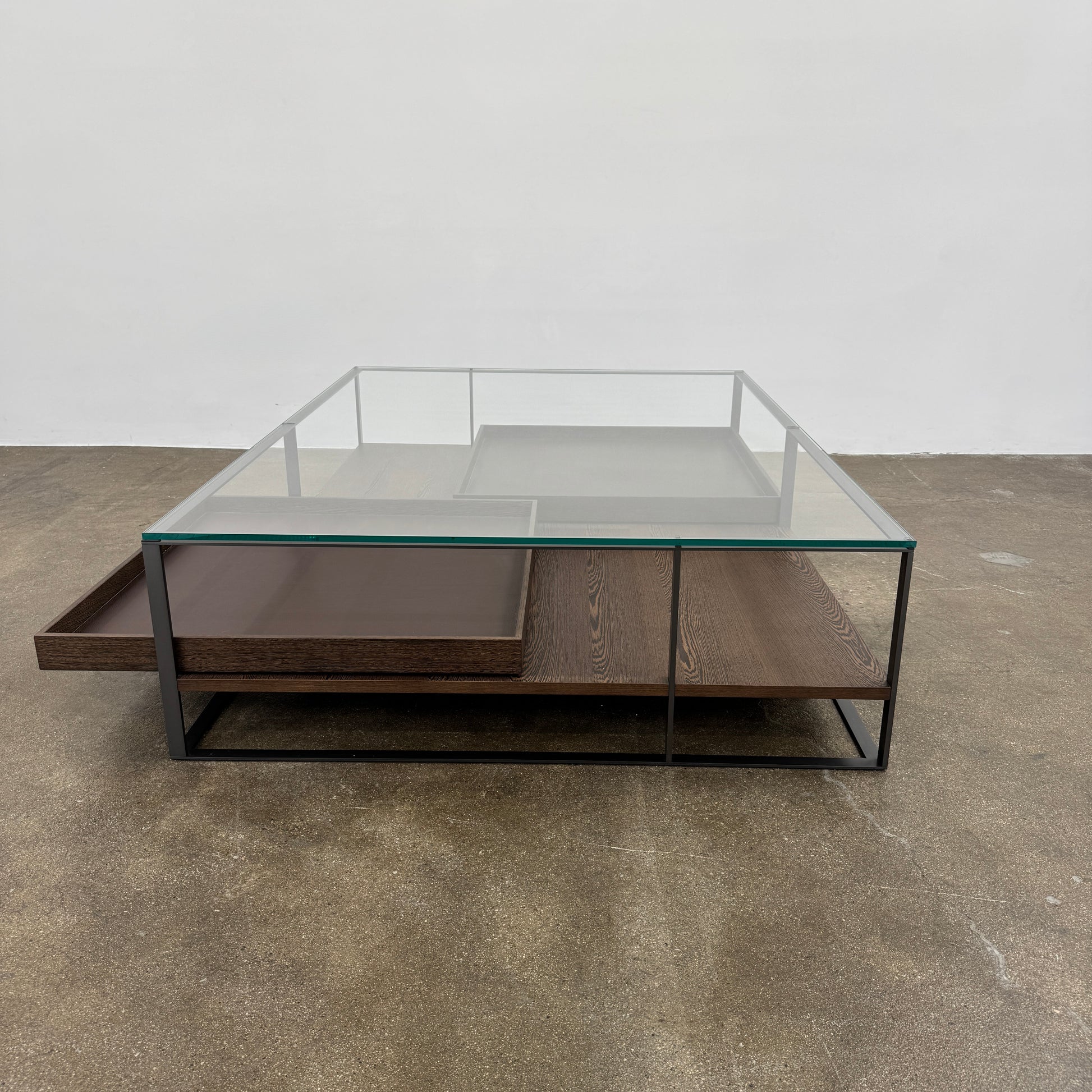 The Maxalto Lithos Coffee Table by Maxalto features a square metal frame, glass top, and two wooden lower shelves—one slightly raised—inspired by the original design. Shown against a plain white background.