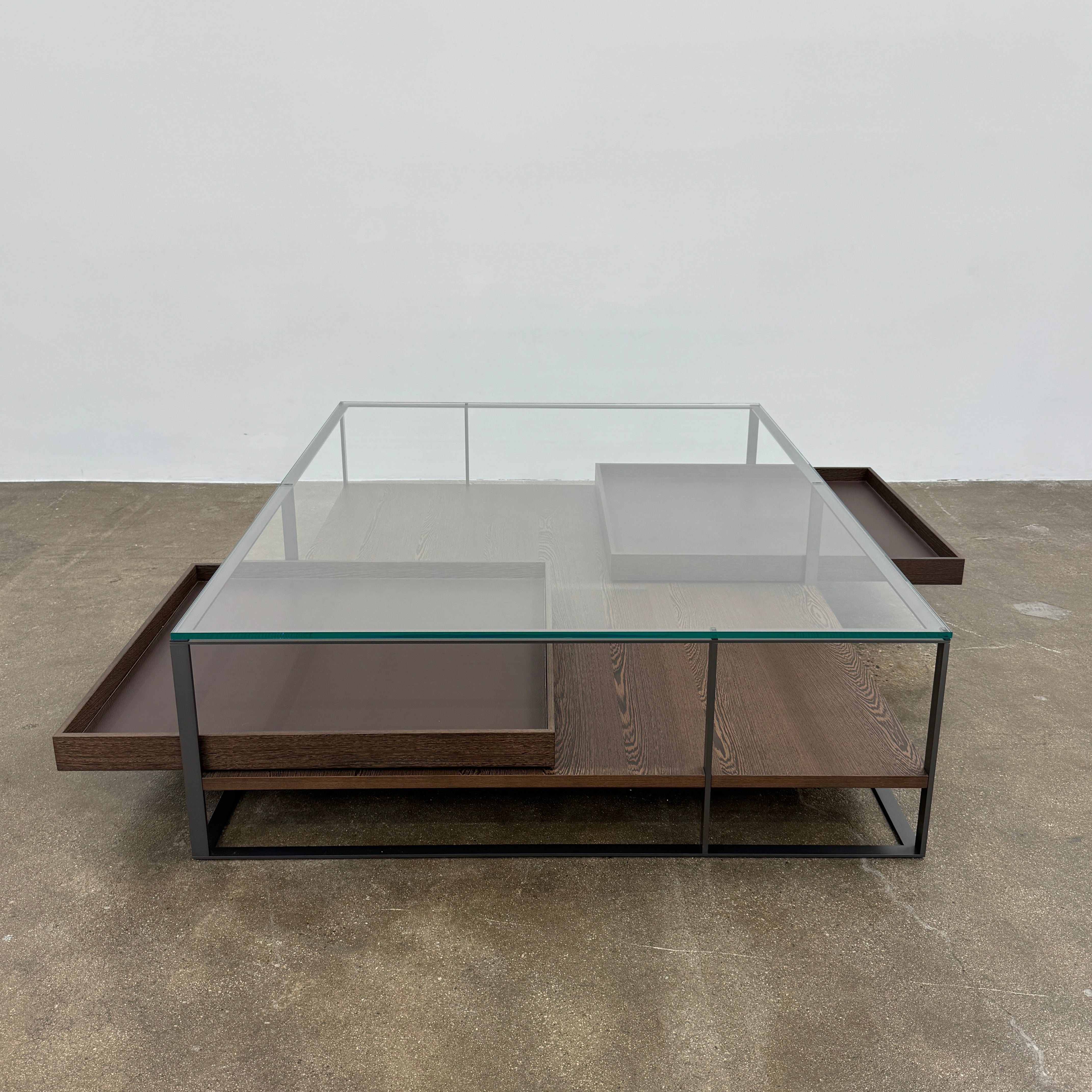 The Maxalto Lithos Coffee Table by Maxalto features a square metal frame, glass top, and two wooden lower shelves—one slightly raised—inspired by the original design. Shown against a plain white background.