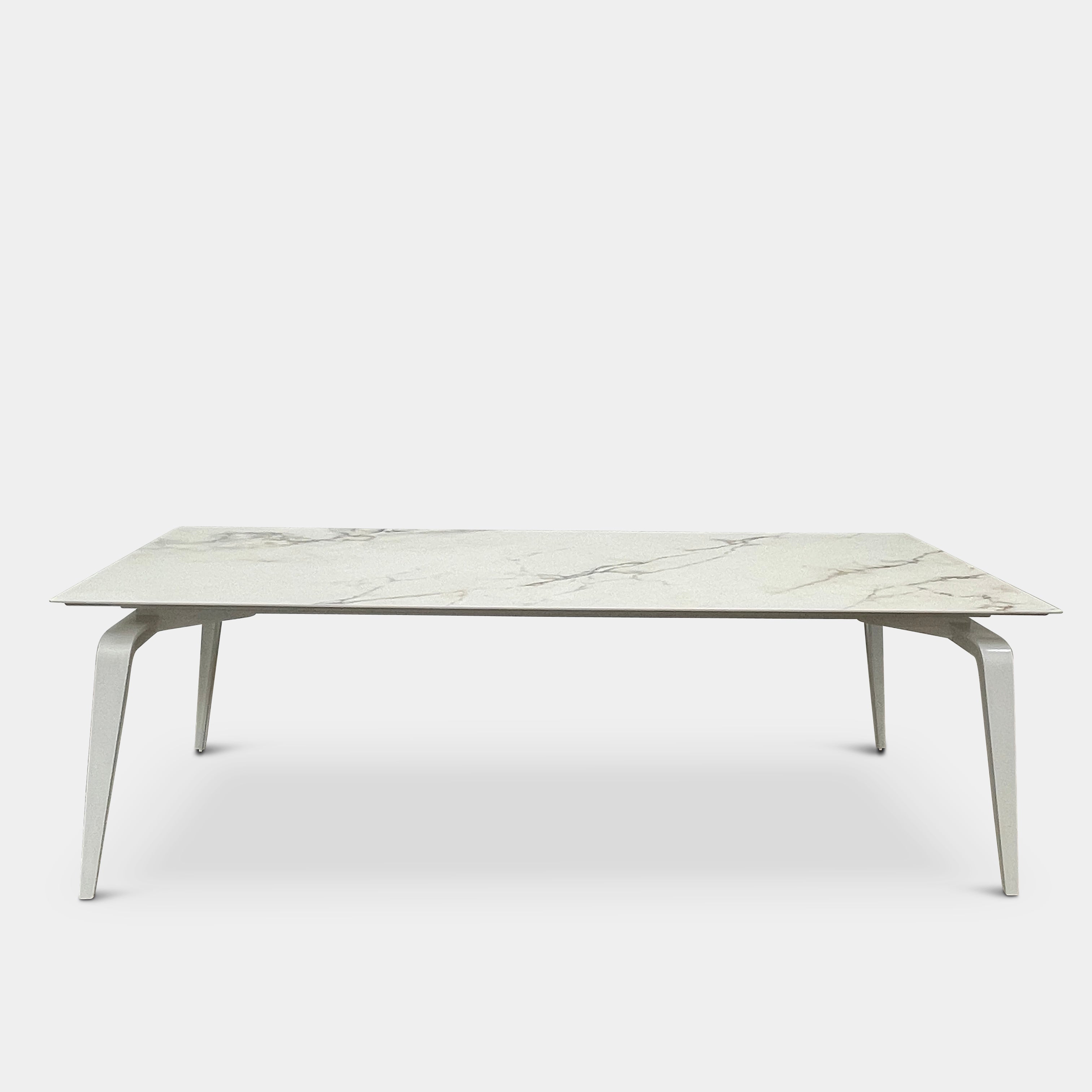 The Ligne Roset Odessa Dining Table showcases a rectangular marble top with angled, folded steel legs, embodying natural minimalism. It is elegantly viewed from the side against a plain background.