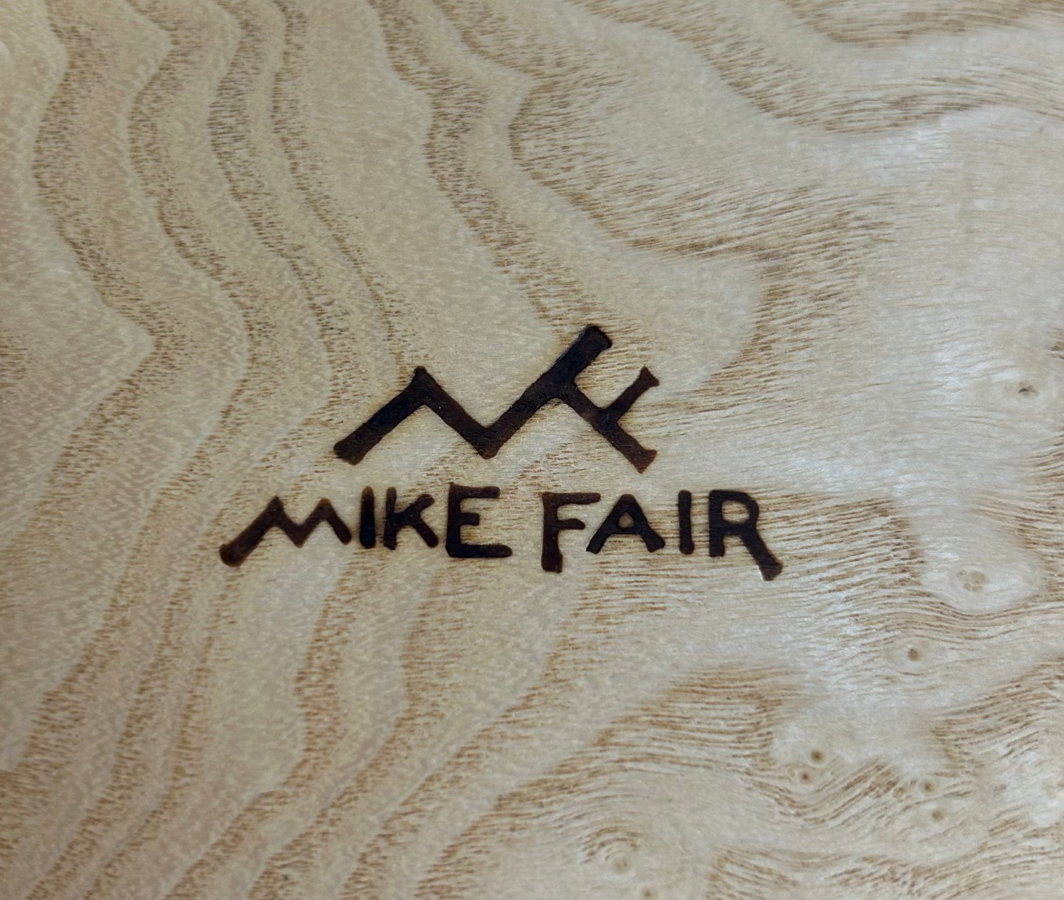 A rectangular table top storage box by Mike Fair Custom Furnishings, crafted from luxurious Macassar Ebony and Ash Burl with a geometric patterned lid, is displayed open to reveal a foam insert inside. The elegant Mike Fair Table Top Storage Box rests on a light fabric surface.
