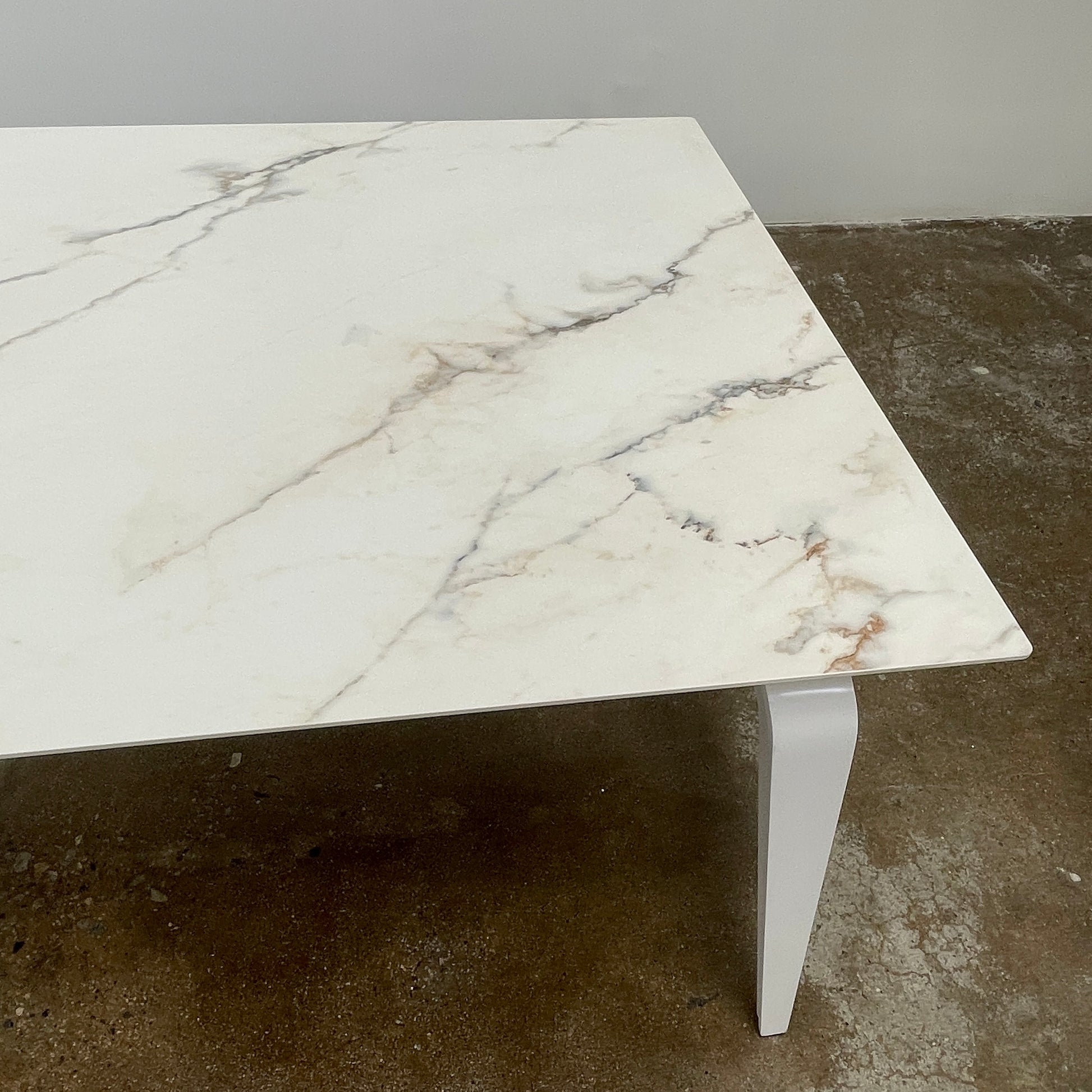 The Ligne Roset Odessa Dining Table showcases a rectangular marble top with angled, folded steel legs, embodying natural minimalism. It is elegantly viewed from the side against a plain background.