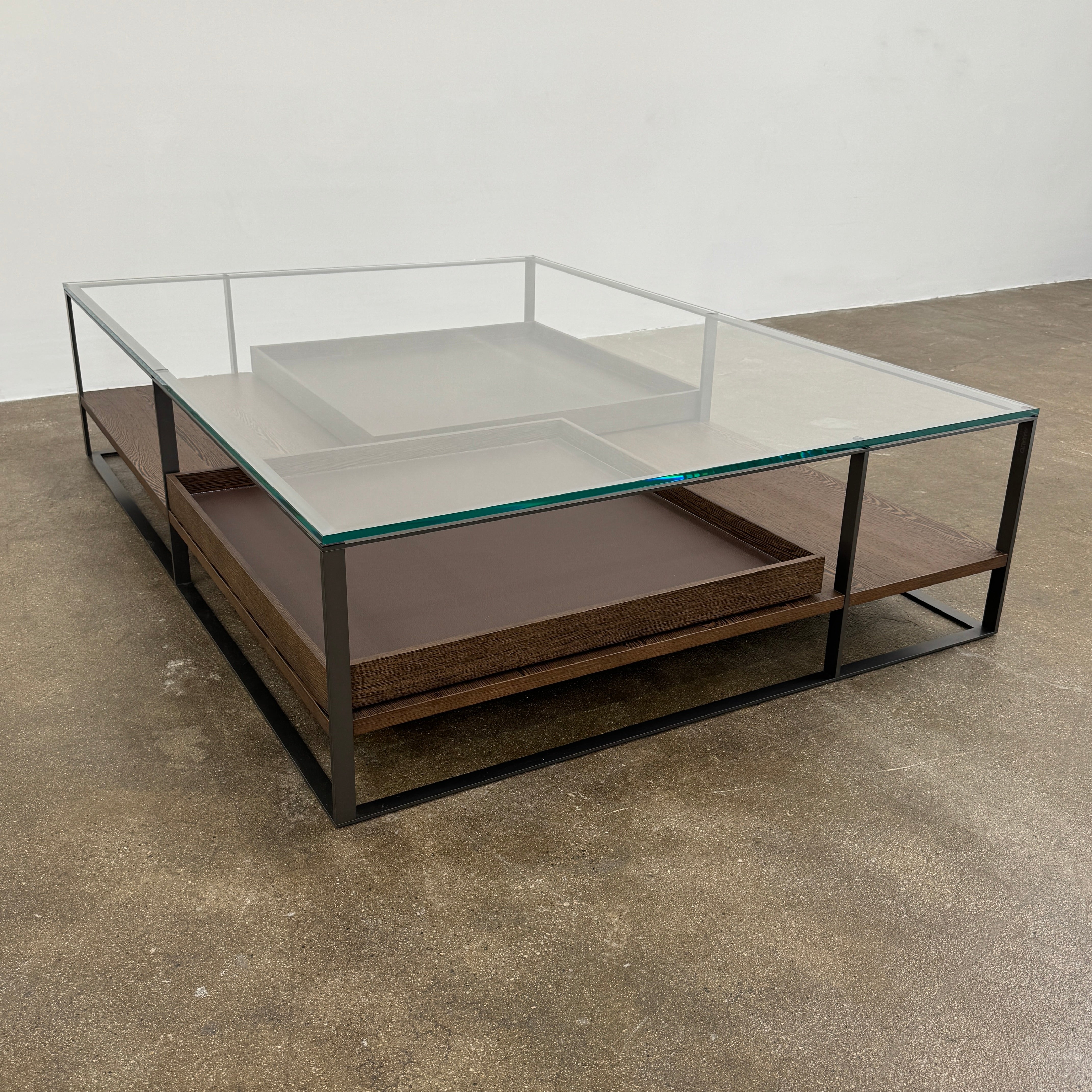 The Maxalto Lithos Coffee Table by Maxalto features a square metal frame, glass top, and two wooden lower shelves—one slightly raised—inspired by the original design. Shown against a plain white background.