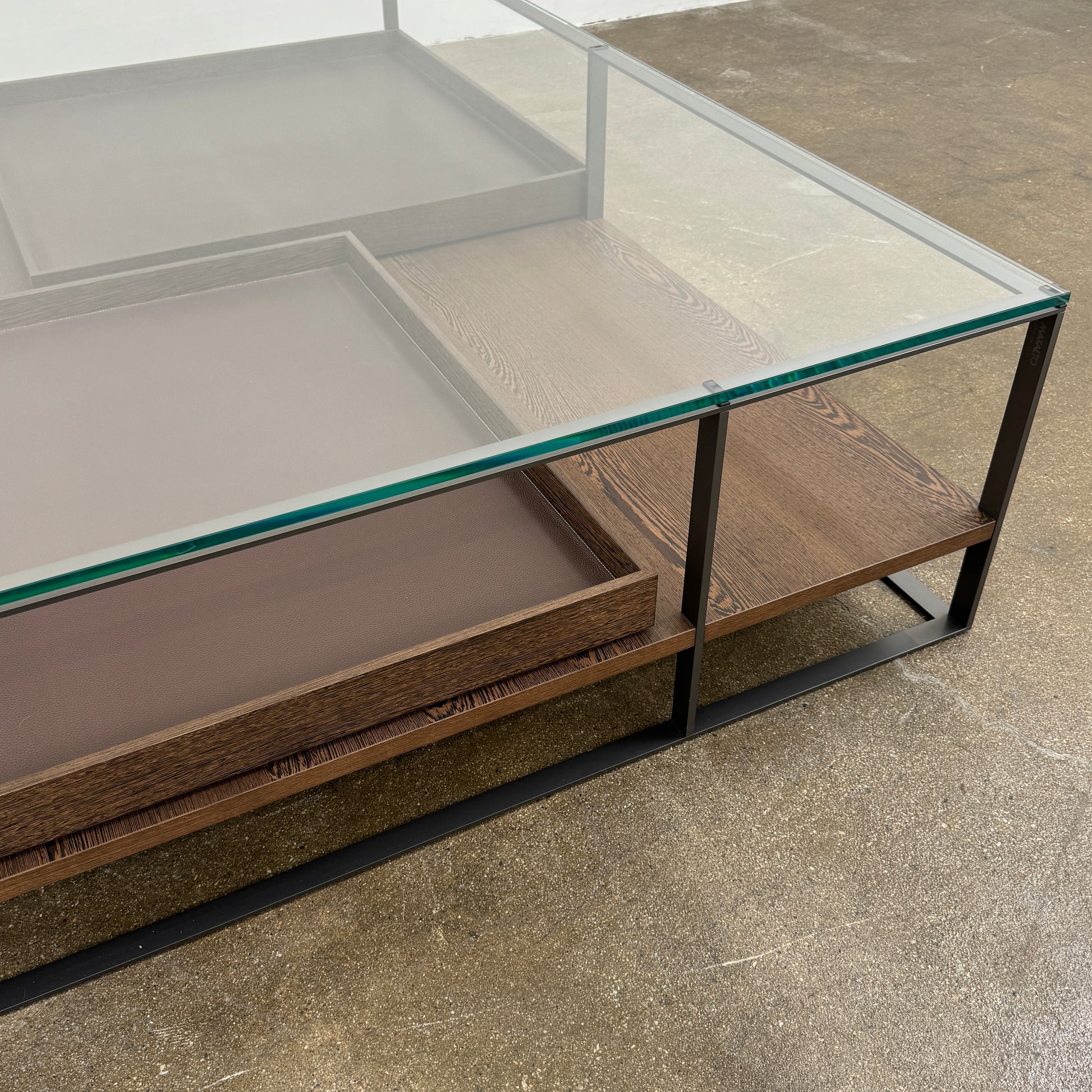The Maxalto Lithos Coffee Table by Maxalto features a square metal frame, glass top, and two wooden lower shelves—one slightly raised—inspired by the original design. Shown against a plain white background.
