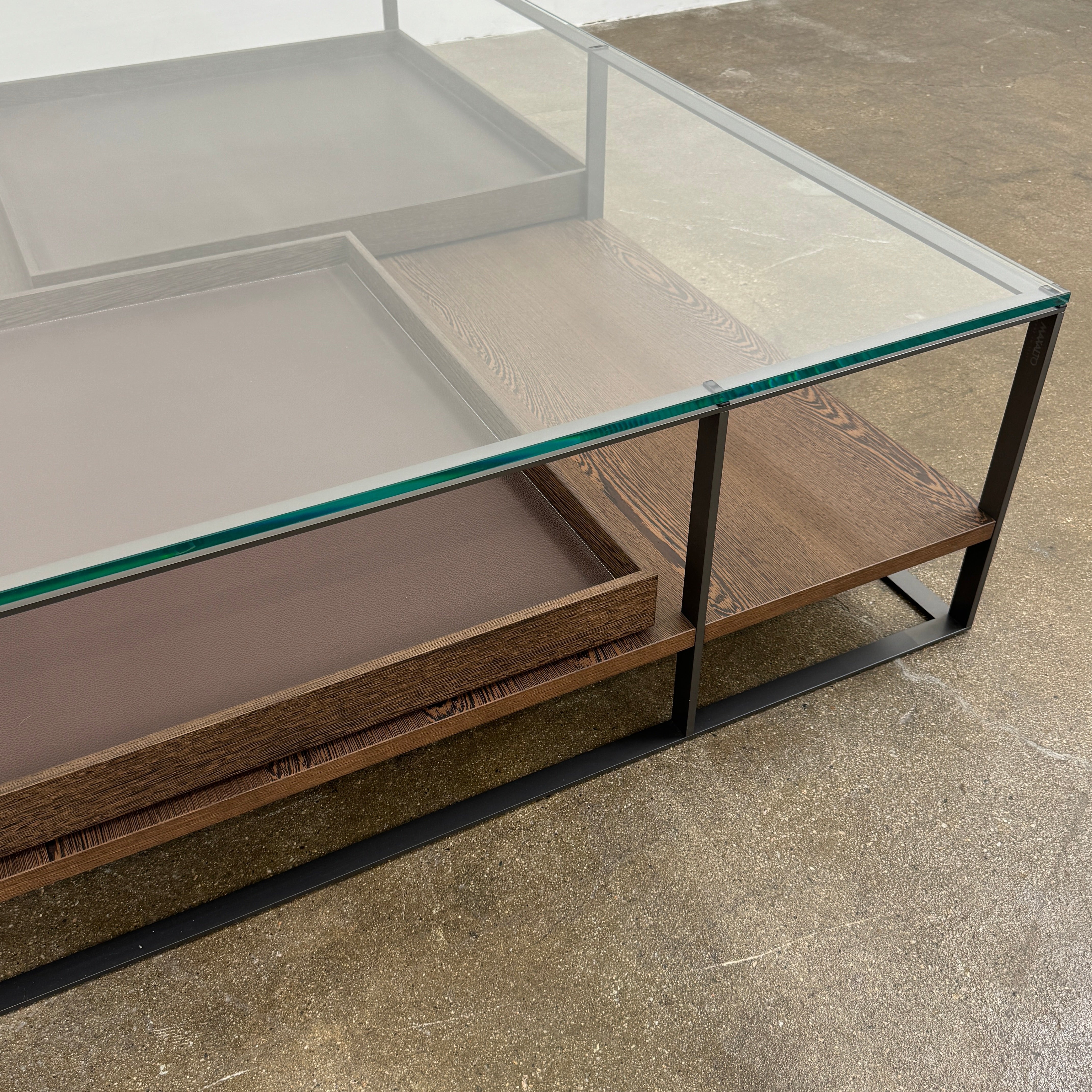 The Maxalto Lithos Coffee Table by Maxalto features a square metal frame, glass top, and two wooden lower shelves—one slightly raised—inspired by the original design. Shown against a plain white background.