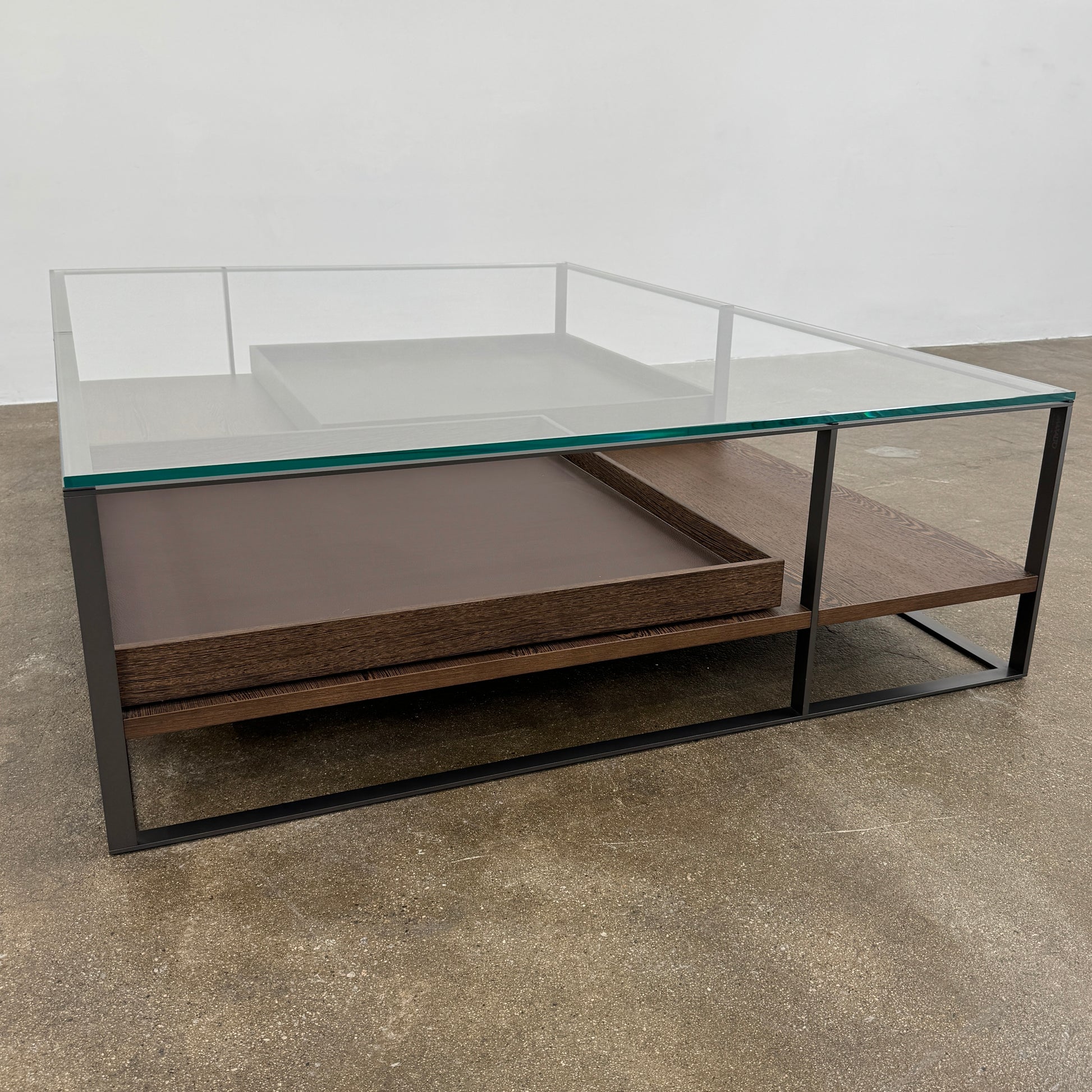 The Maxalto Lithos Coffee Table by Maxalto features a square metal frame, glass top, and two wooden lower shelves—one slightly raised—inspired by the original design. Shown against a plain white background.