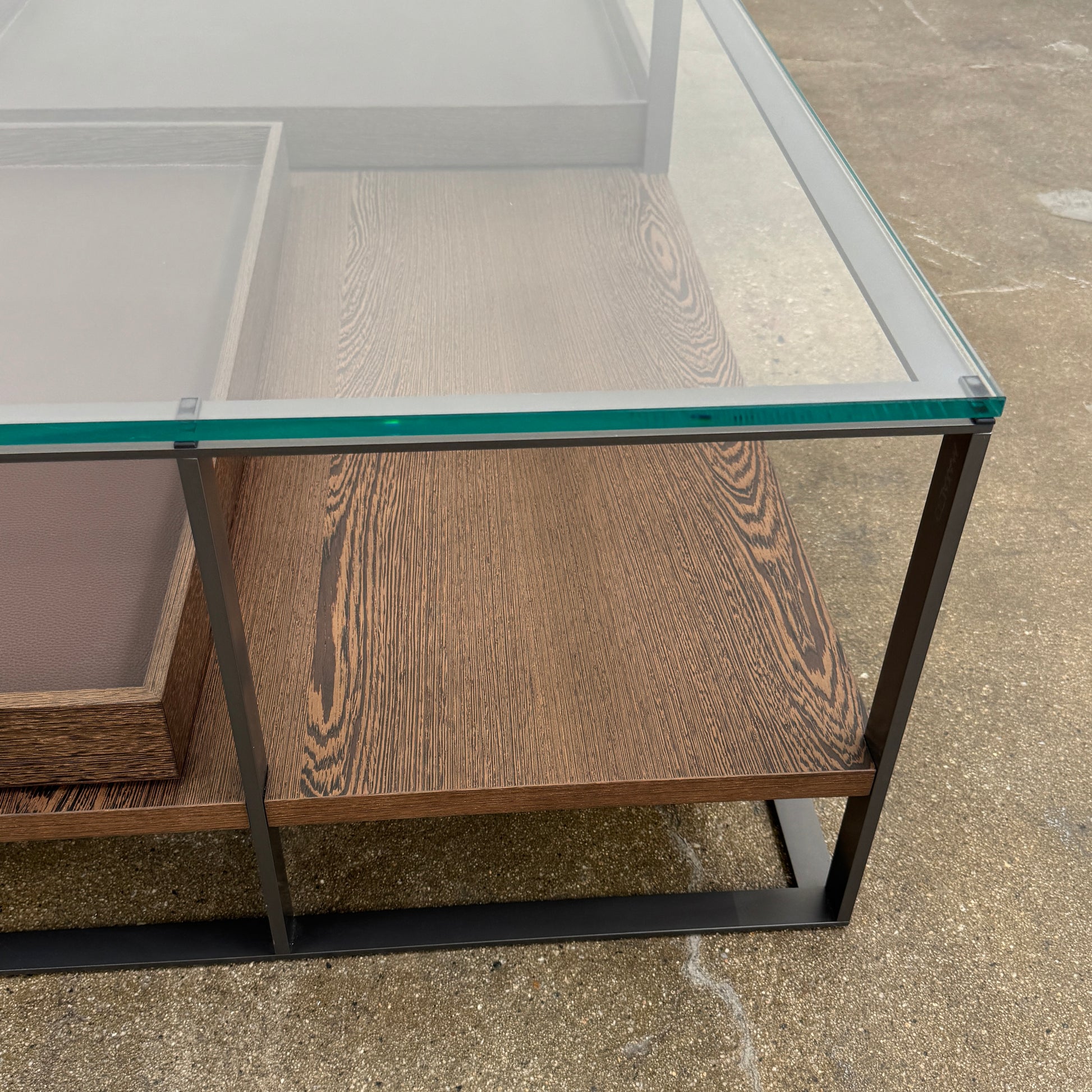 The Maxalto Lithos Coffee Table by Maxalto features a square metal frame, glass top, and two wooden lower shelves—one slightly raised—inspired by the original design. Shown against a plain white background.