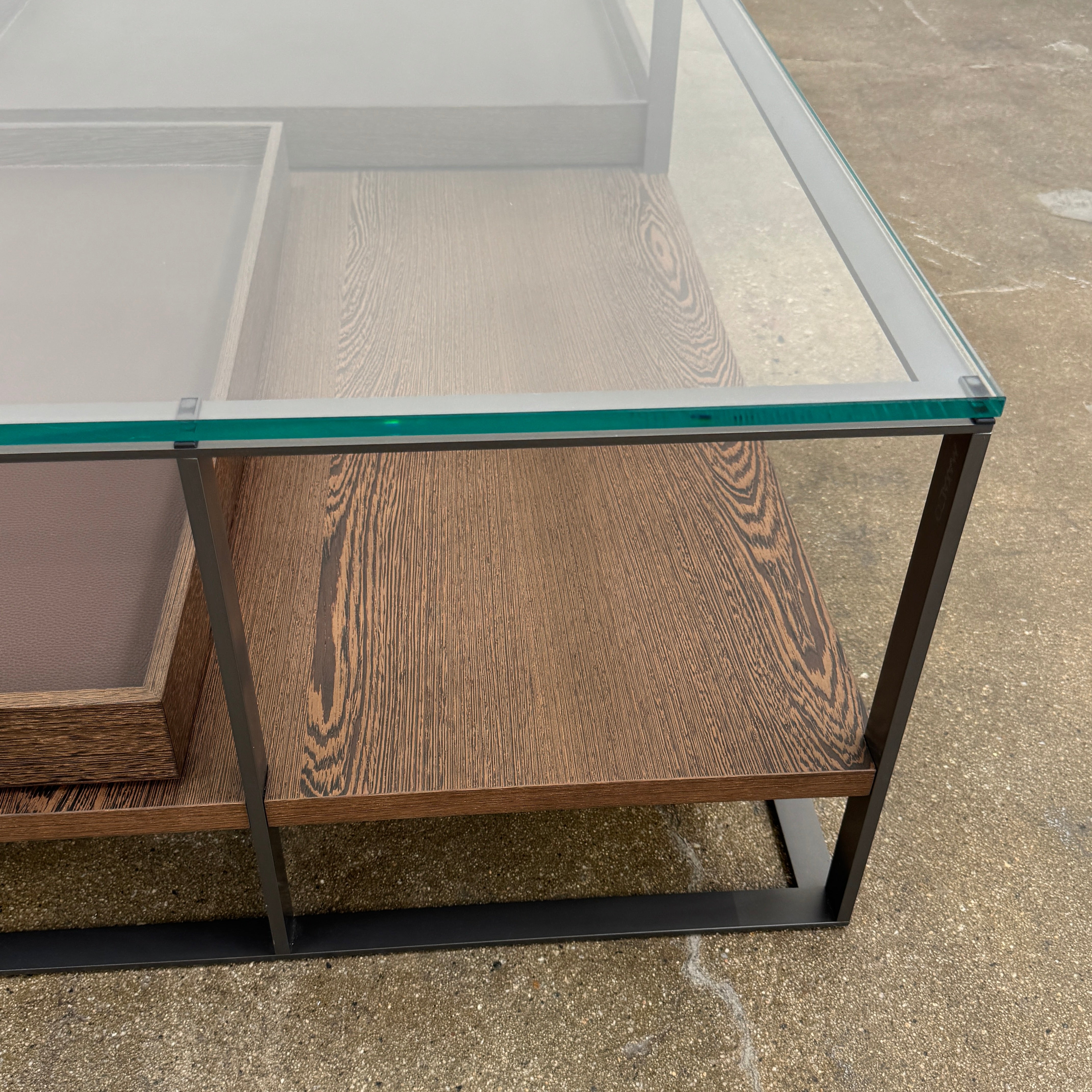 The Maxalto Lithos Coffee Table by Maxalto features a square metal frame, glass top, and two wooden lower shelves—one slightly raised—inspired by the original design. Shown against a plain white background.