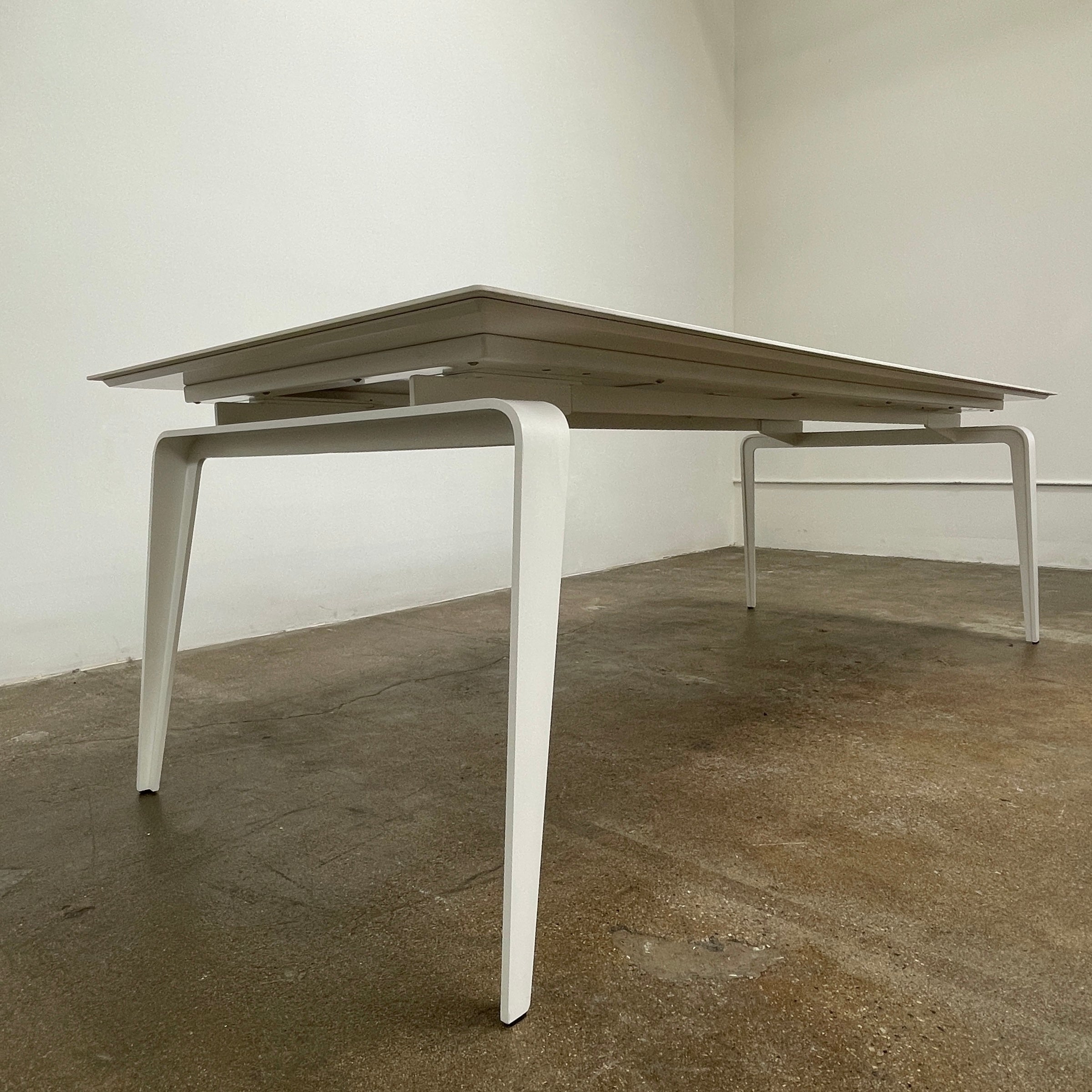 The Ligne Roset Odessa Dining Table showcases a rectangular marble top with angled, folded steel legs, embodying natural minimalism. It is elegantly viewed from the side against a plain background.