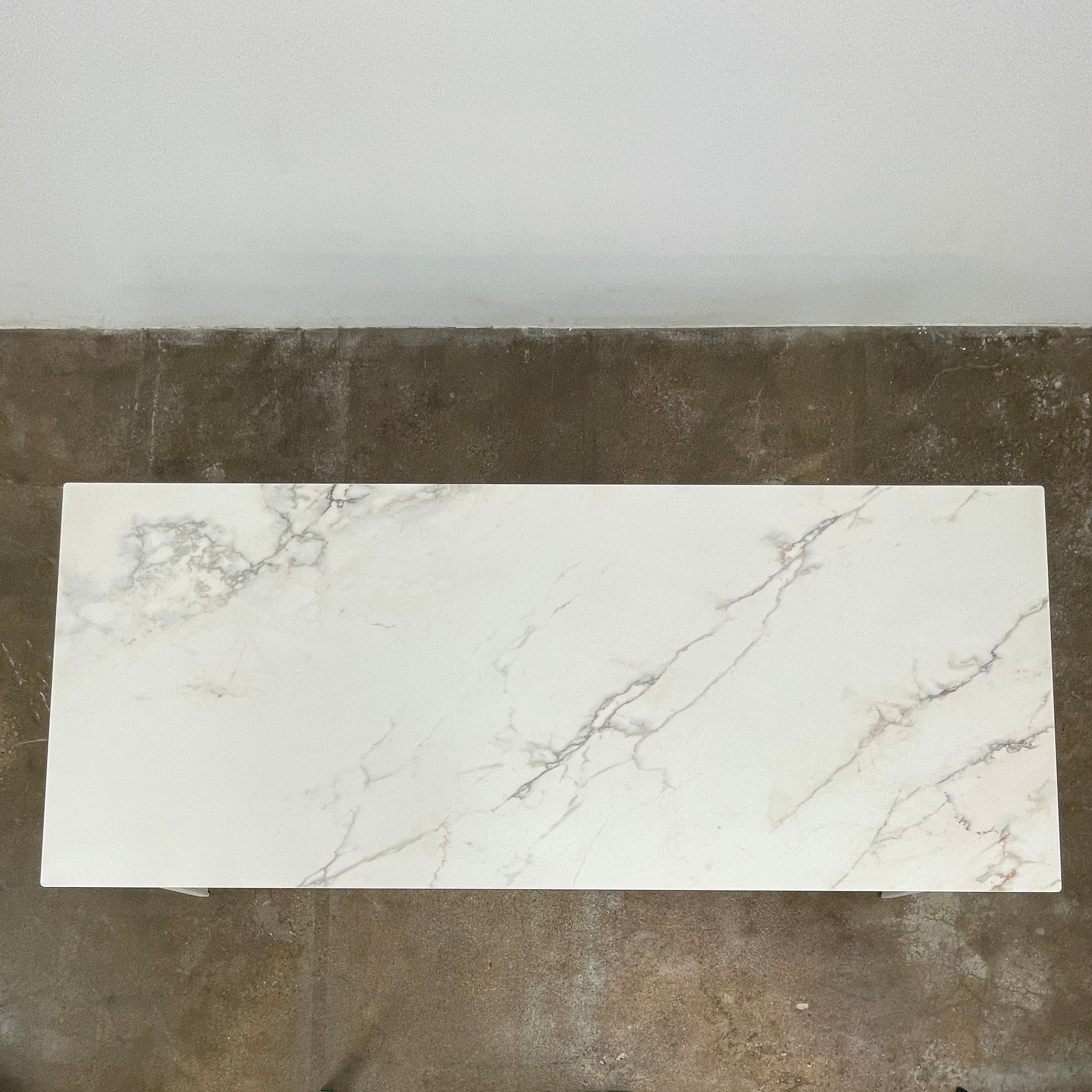 The Ligne Roset Odessa Dining Table showcases a rectangular marble top with angled, folded steel legs, embodying natural minimalism. It is elegantly viewed from the side against a plain background.