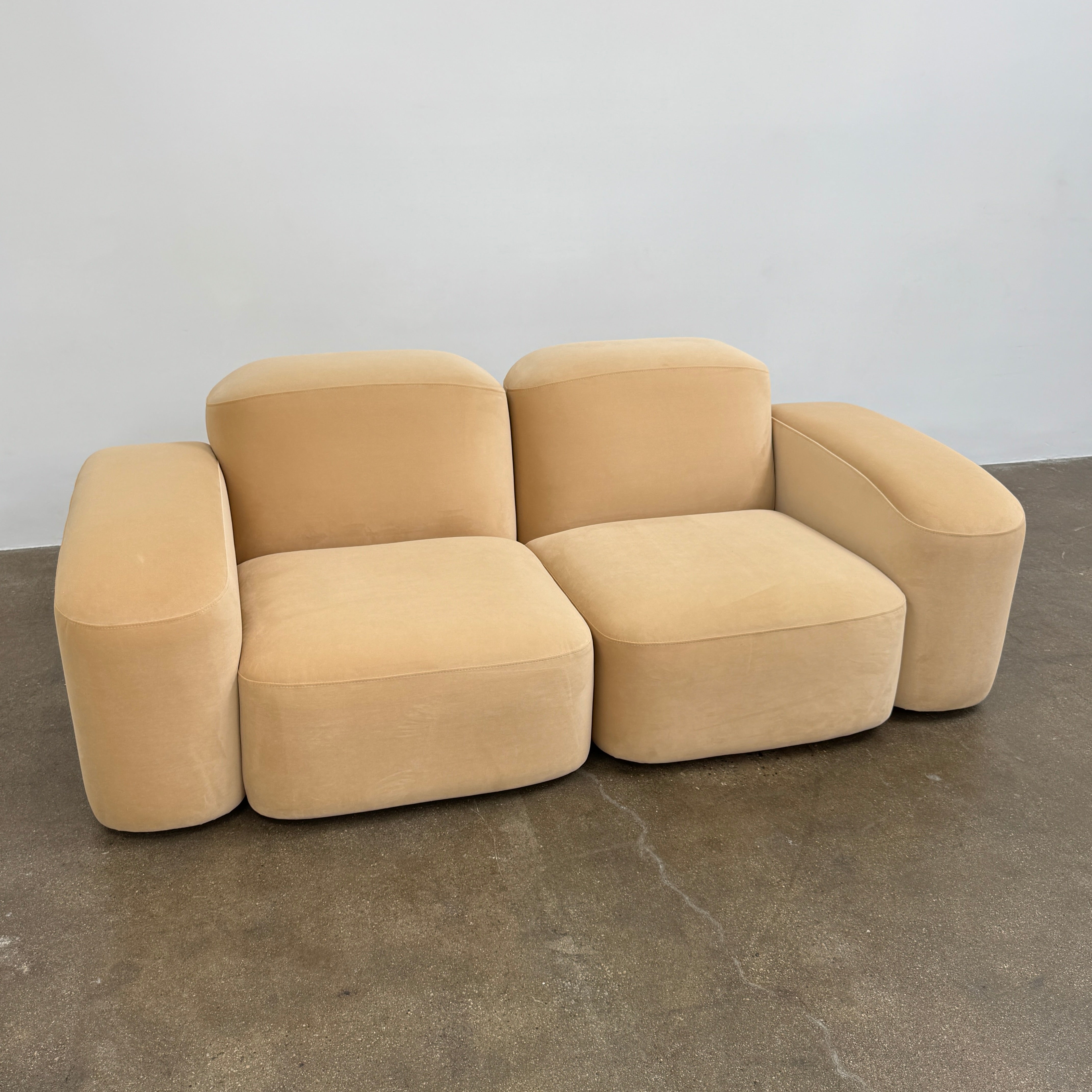The Ellison Studios “Muse” Sofa Two Seater, in modern beige with plush rounded cushions and arms, channels Sarah Ellison’s signature style, shown here on a polished concrete floor against a plain light wall.