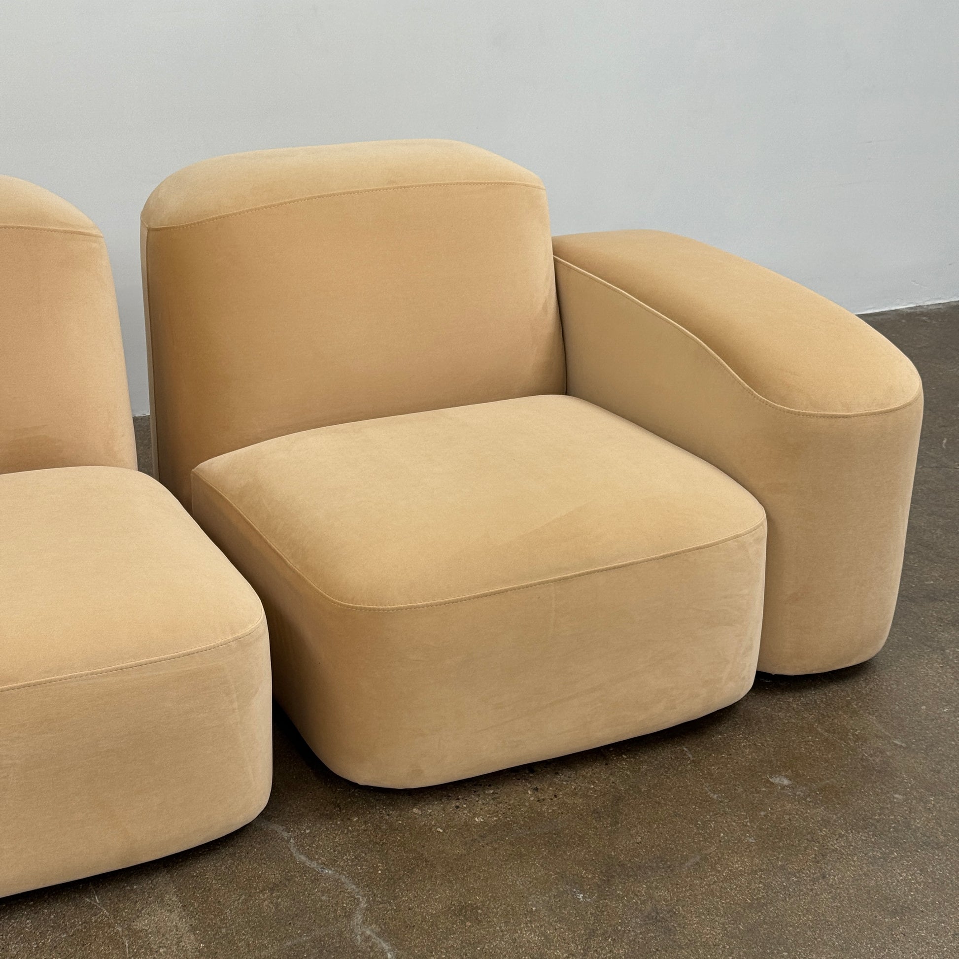 The Ellison Studios “Muse” Sofa Two Seater, in modern beige with plush rounded cushions and arms, channels Sarah Ellison’s signature style, shown here on a polished concrete floor against a plain light wall.