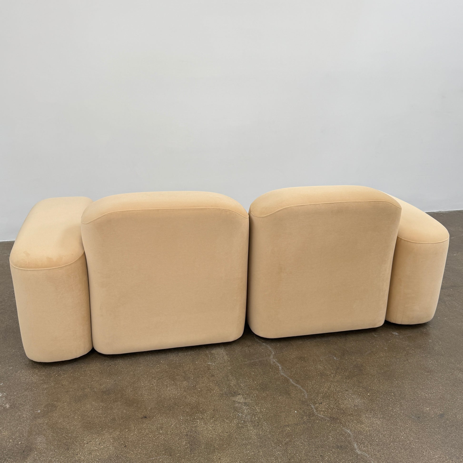 The Ellison Studios “Muse” Sofa Two Seater, in modern beige with plush rounded cushions and arms, channels Sarah Ellison’s signature style, shown here on a polished concrete floor against a plain light wall.
