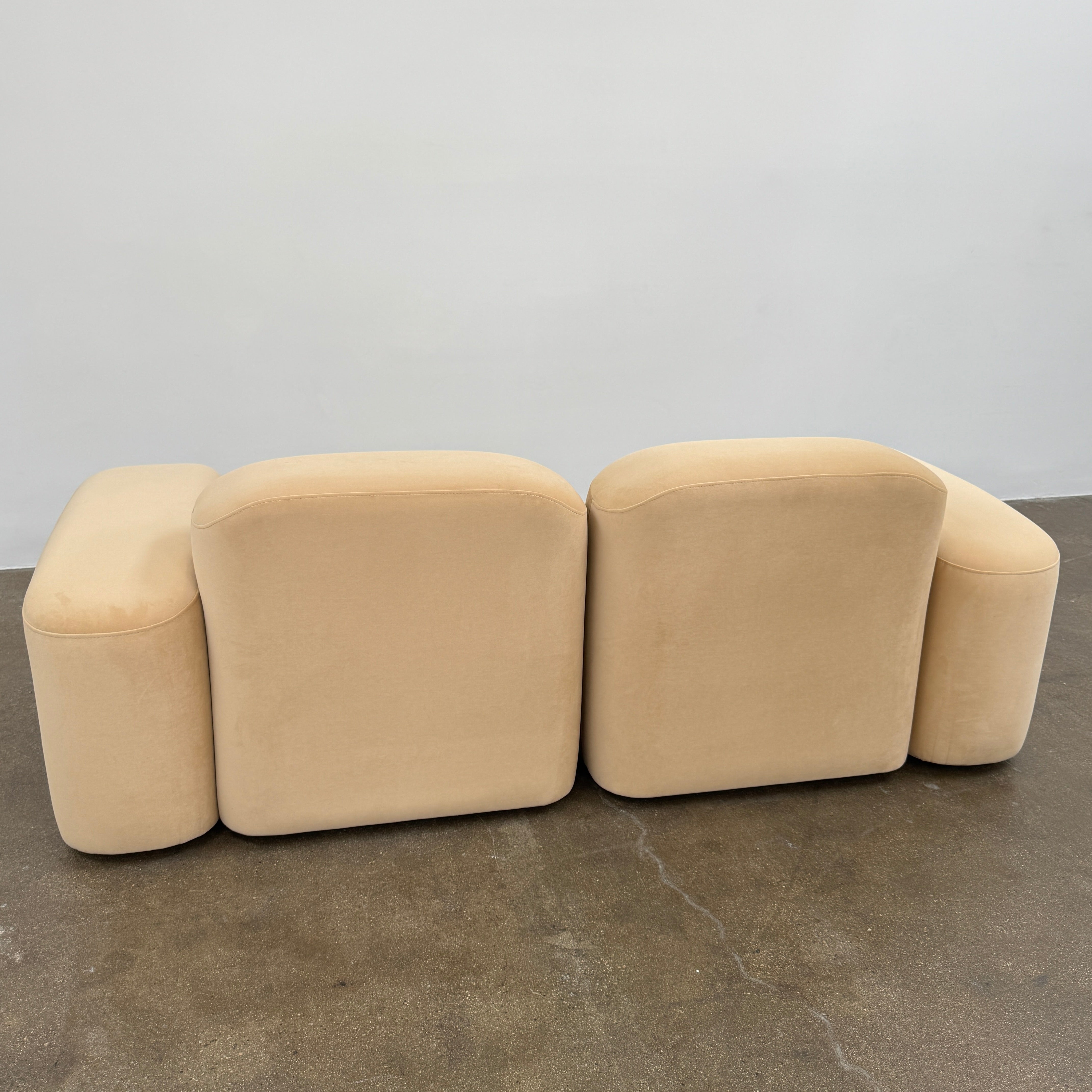 The Ellison Studios “Muse” Sofa Two Seater, in modern beige with plush rounded cushions and arms, channels Sarah Ellison’s signature style, shown here on a polished concrete floor against a plain light wall.