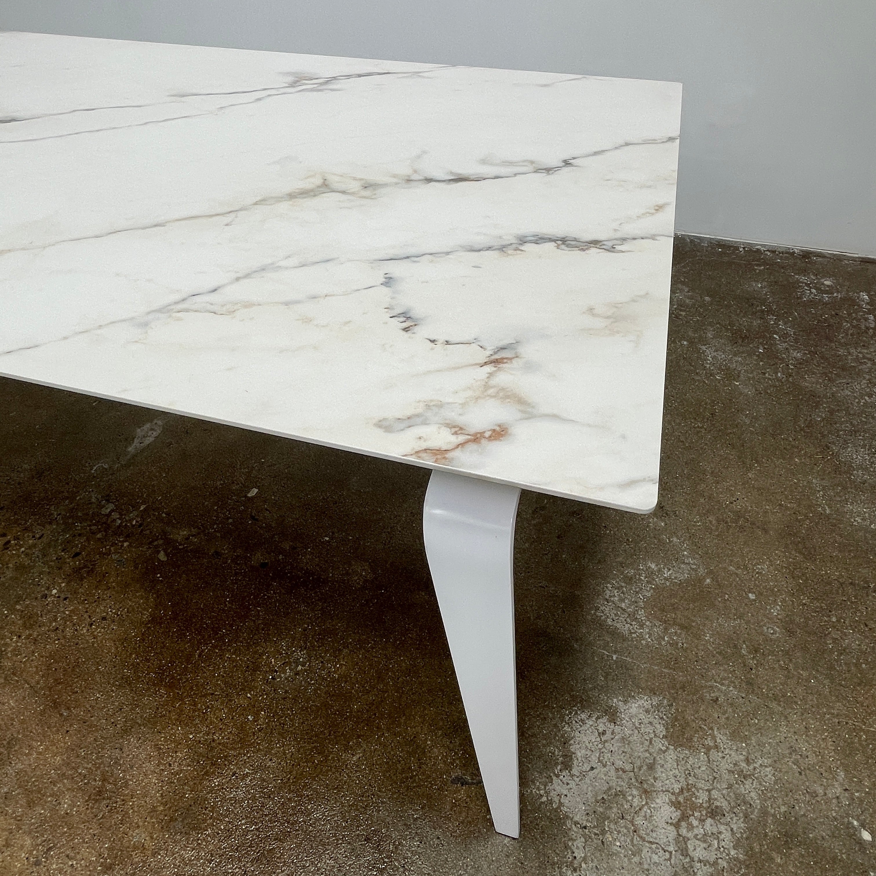 The Ligne Roset Odessa Dining Table showcases a rectangular marble top with angled, folded steel legs, embodying natural minimalism. It is elegantly viewed from the side against a plain background.