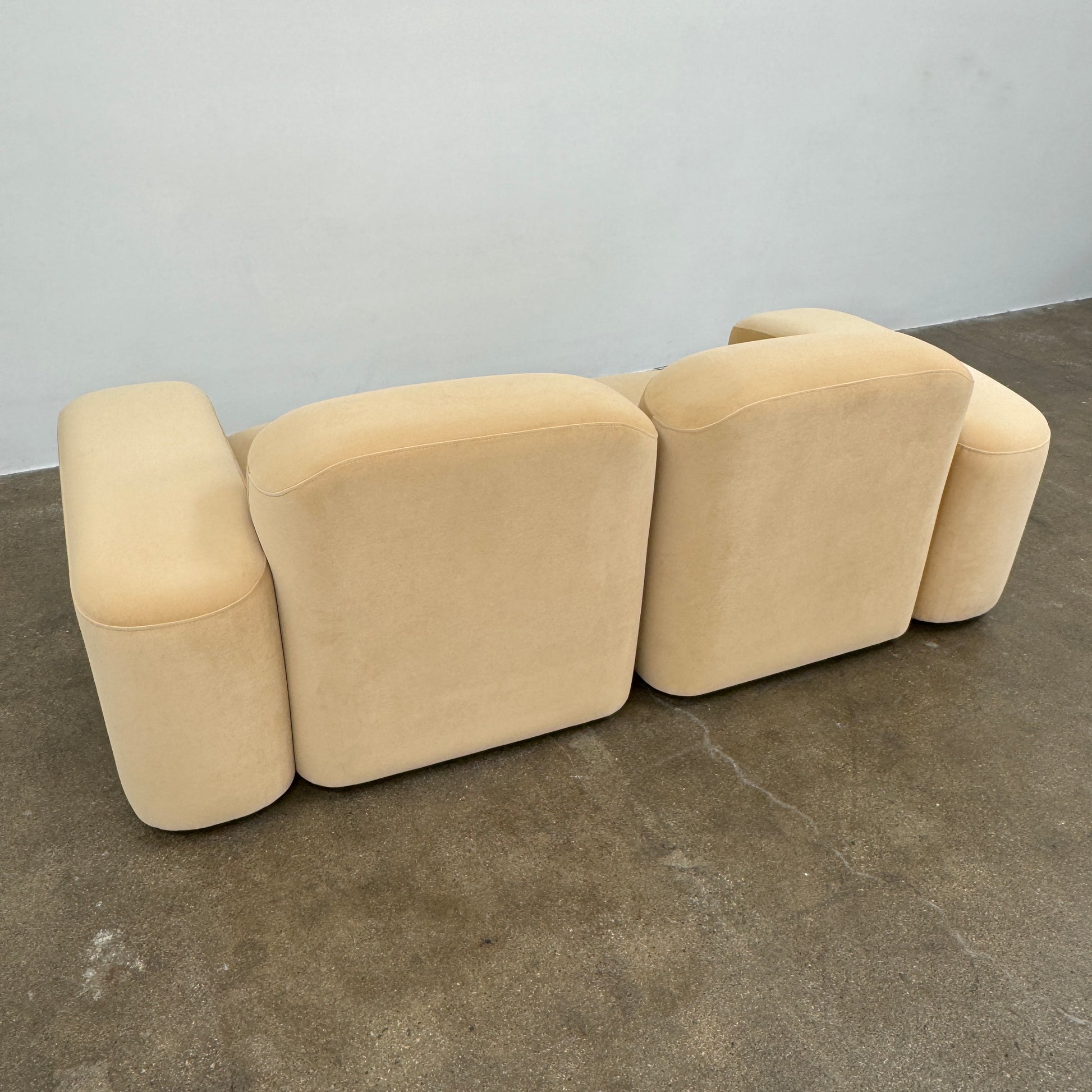 The Ellison Studios “Muse” Sofa Two Seater, in modern beige with plush rounded cushions and arms, channels Sarah Ellison’s signature style, shown here on a polished concrete floor against a plain light wall.