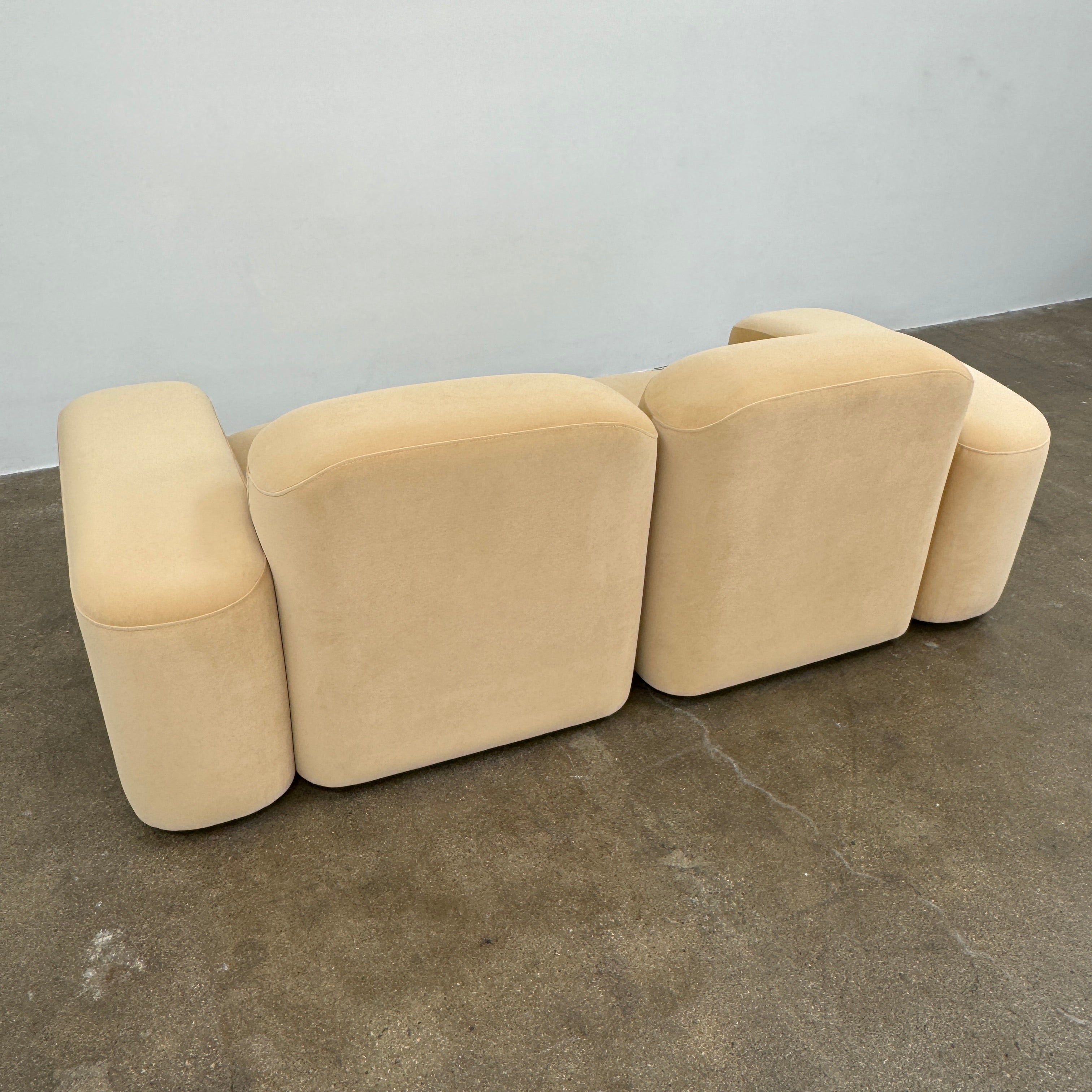 The Ellison Studios “Muse” Sofa Two Seater, in modern beige with plush rounded cushions and arms, channels Sarah Ellison’s signature style, shown here on a polished concrete floor against a plain light wall.