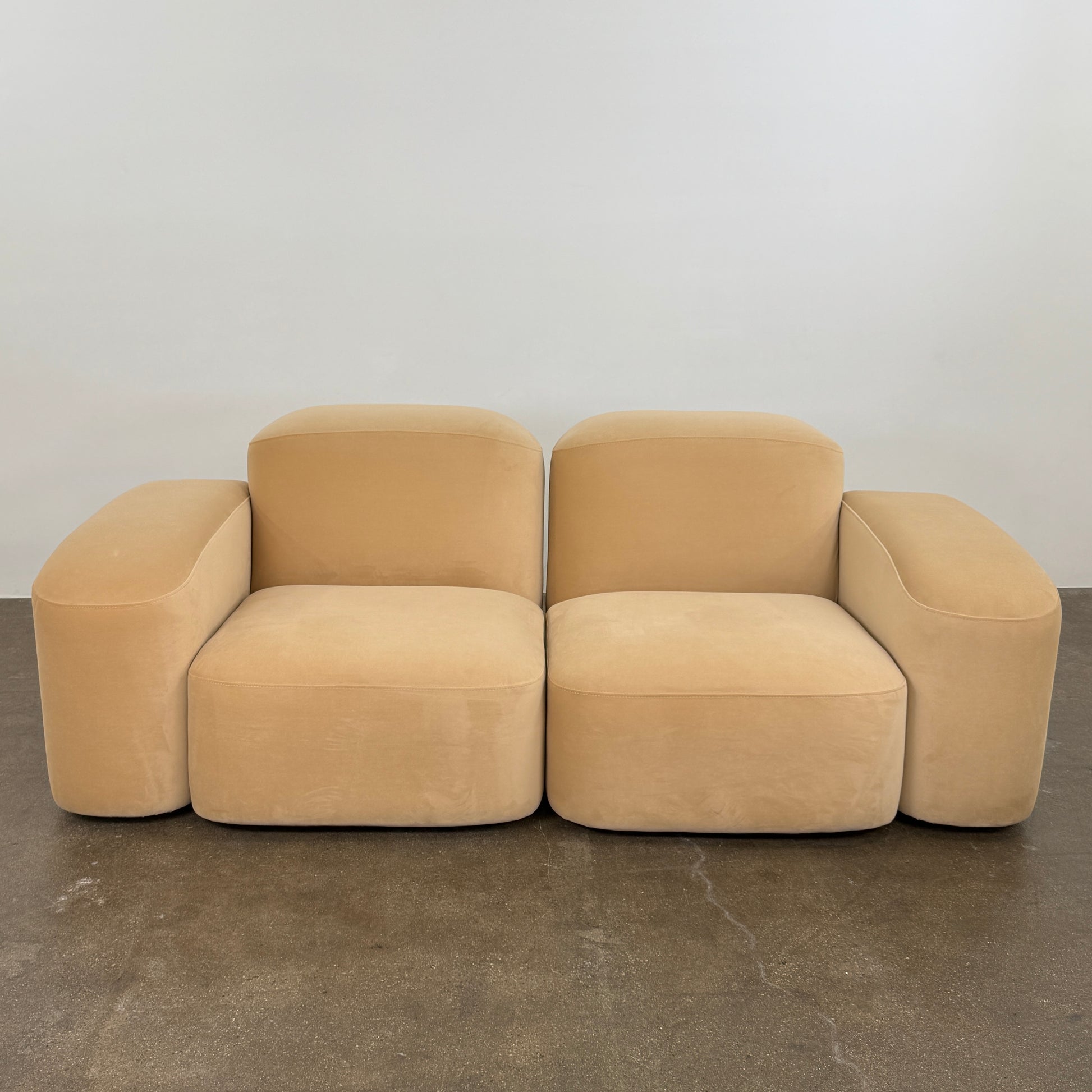 The Ellison Studios “Muse” Sofa Two Seater, in modern beige with plush rounded cushions and arms, channels Sarah Ellison’s signature style, shown here on a polished concrete floor against a plain light wall.