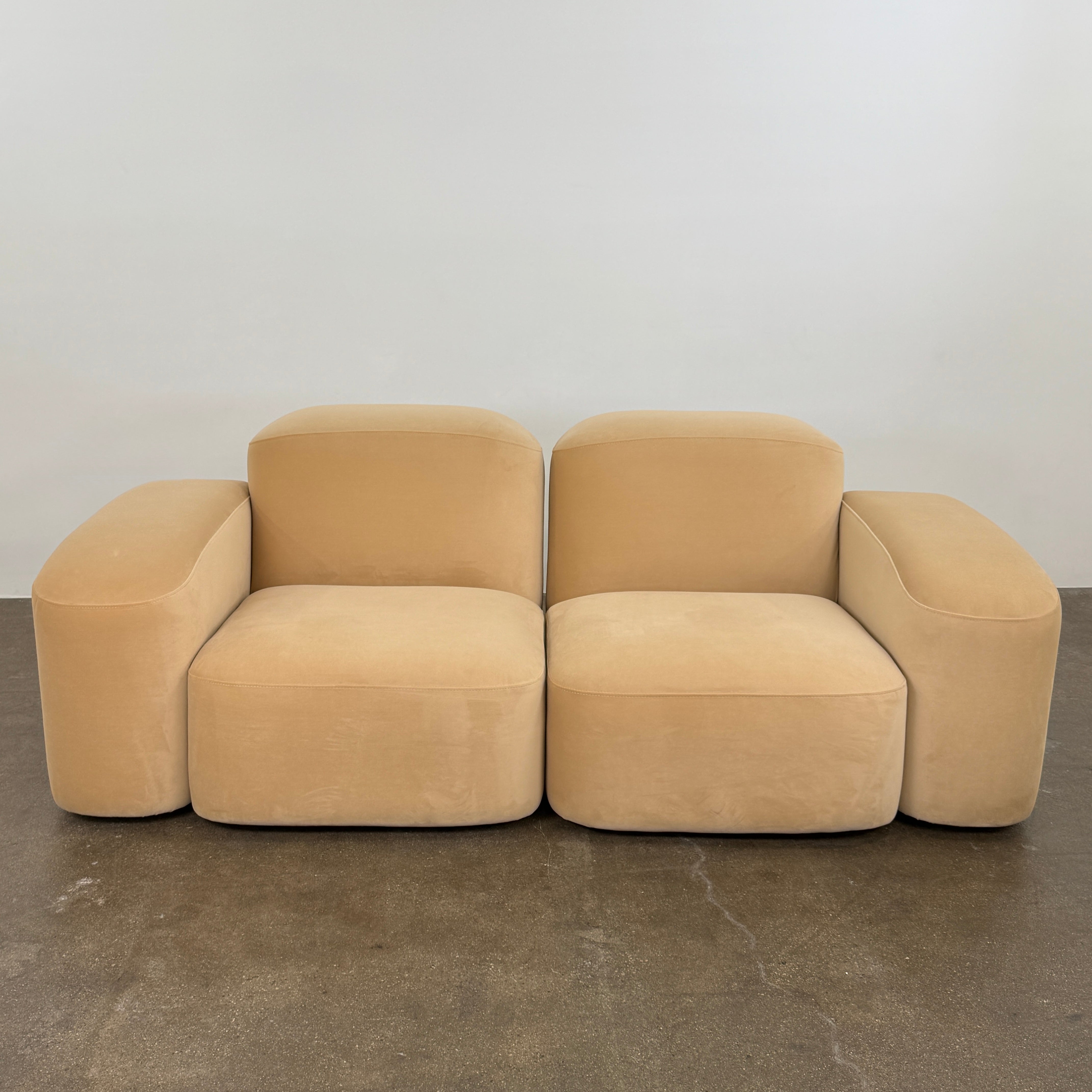 The Ellison Studios “Muse” Sofa Two Seater, in modern beige with plush rounded cushions and arms, channels Sarah Ellison’s signature style, shown here on a polished concrete floor against a plain light wall.
