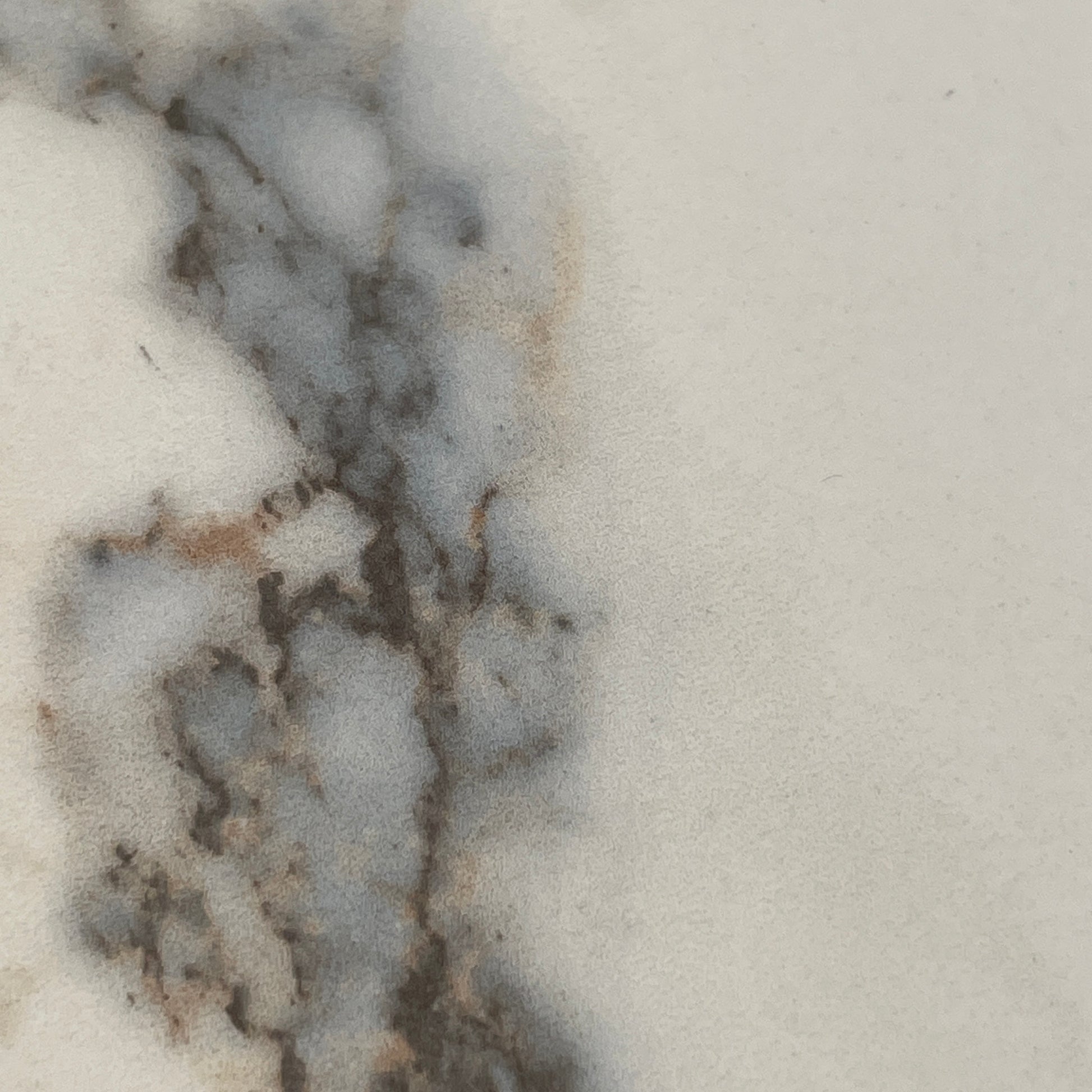 The Ligne Roset Odessa Dining Table showcases a rectangular marble top with angled, folded steel legs, embodying natural minimalism. It is elegantly viewed from the side against a plain background.