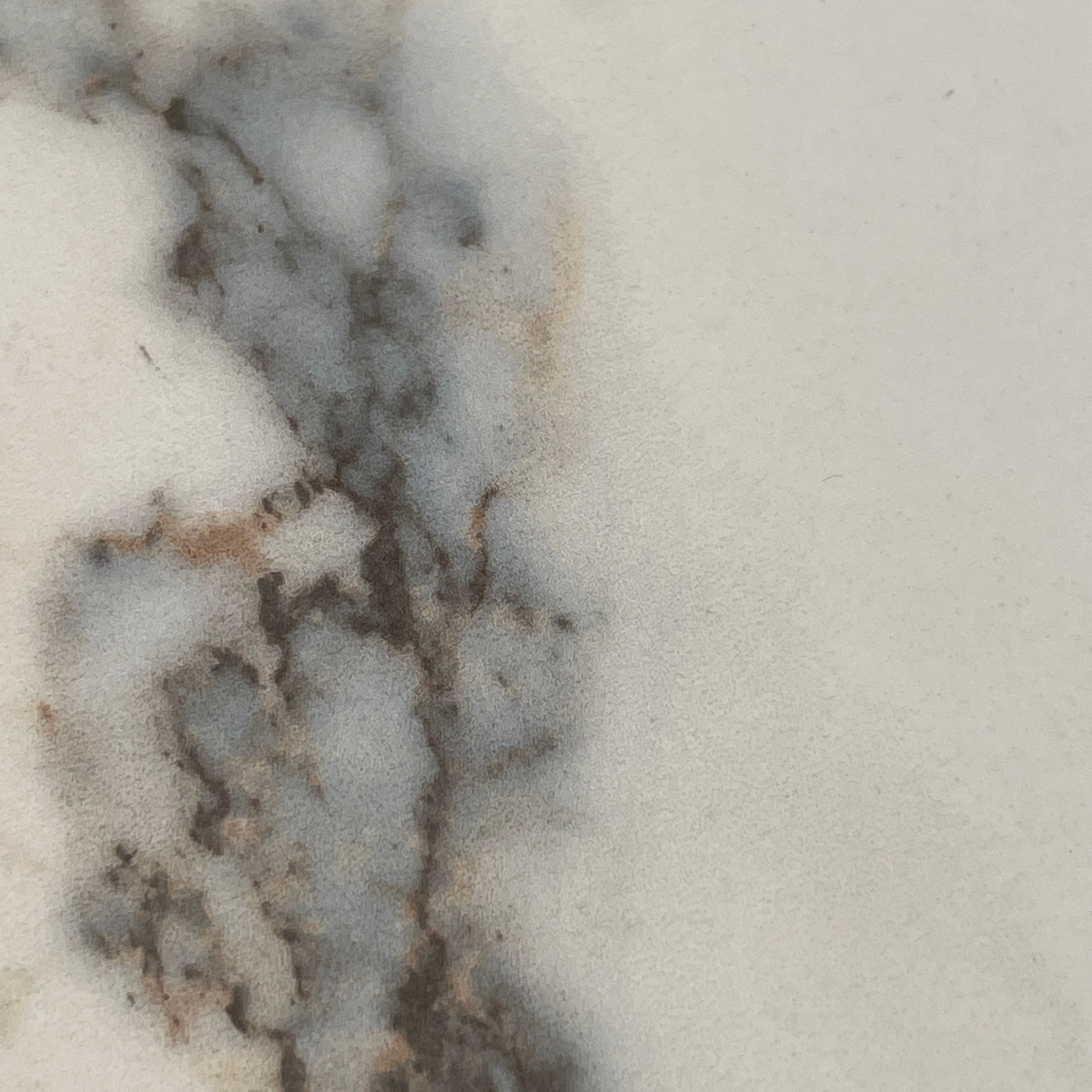 The Ligne Roset Odessa Dining Table showcases a rectangular marble top with angled, folded steel legs, embodying natural minimalism. It is elegantly viewed from the side against a plain background.