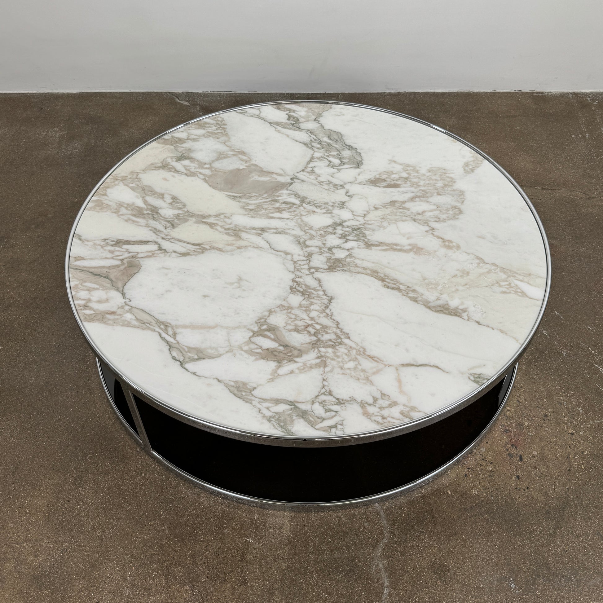 The Minotti Huber Coffee Table by Minotti features a round design with a white statuary marble top, dark lower shelf, and sleek metal frame, set against a plain light background.