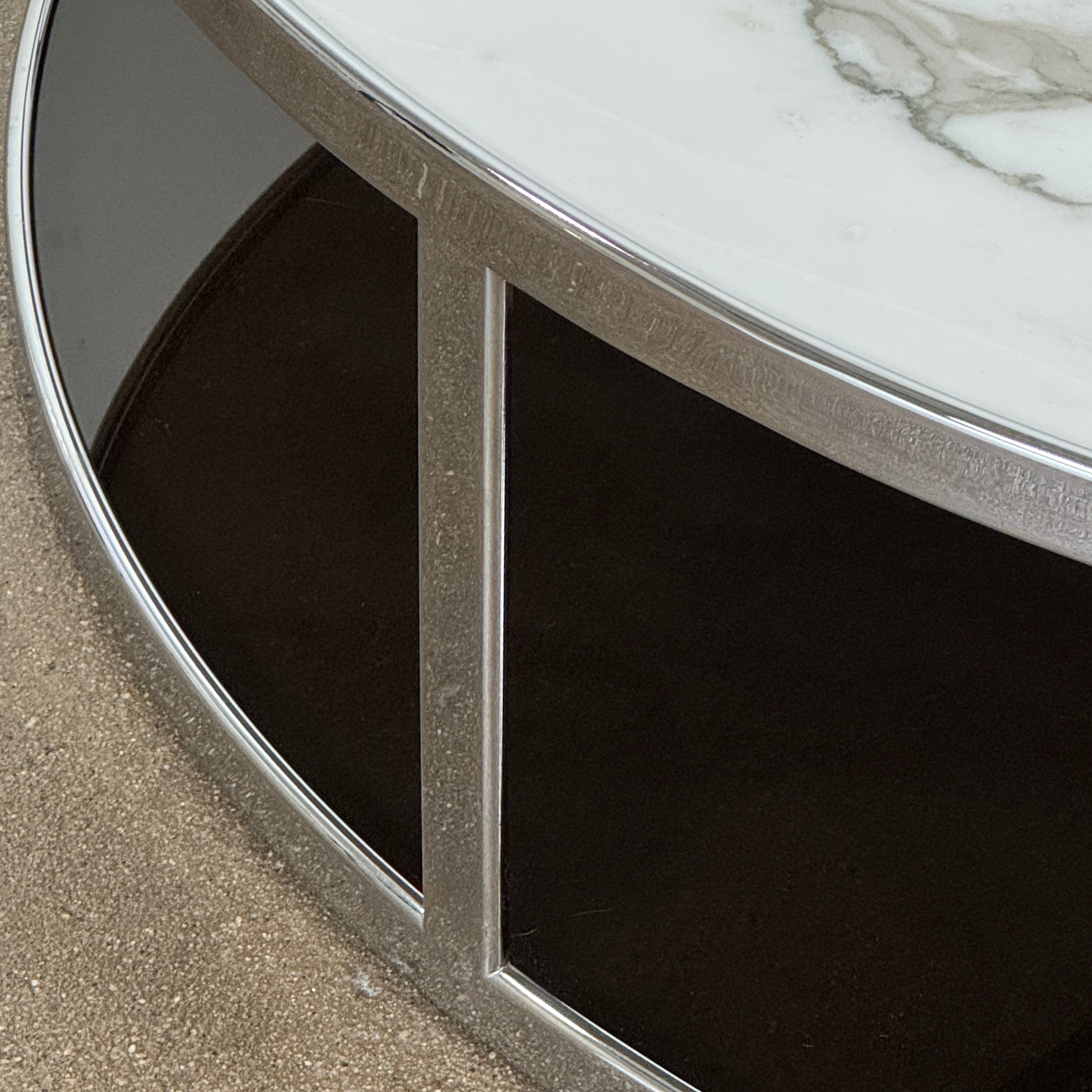 The Minotti Huber Coffee Table by Minotti features a round design with a white statuary marble top, dark lower shelf, and sleek metal frame, set against a plain light background.