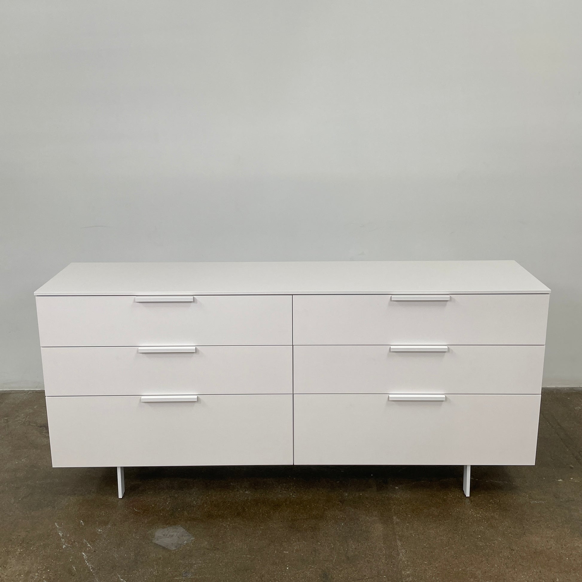 The Modern Resale Ligne Roset Everywhere 6 Drawer Dresser is a white, minimalist piece with sleek metal handles and two sturdy metal legs, elegantly presented in front of a plain white background.