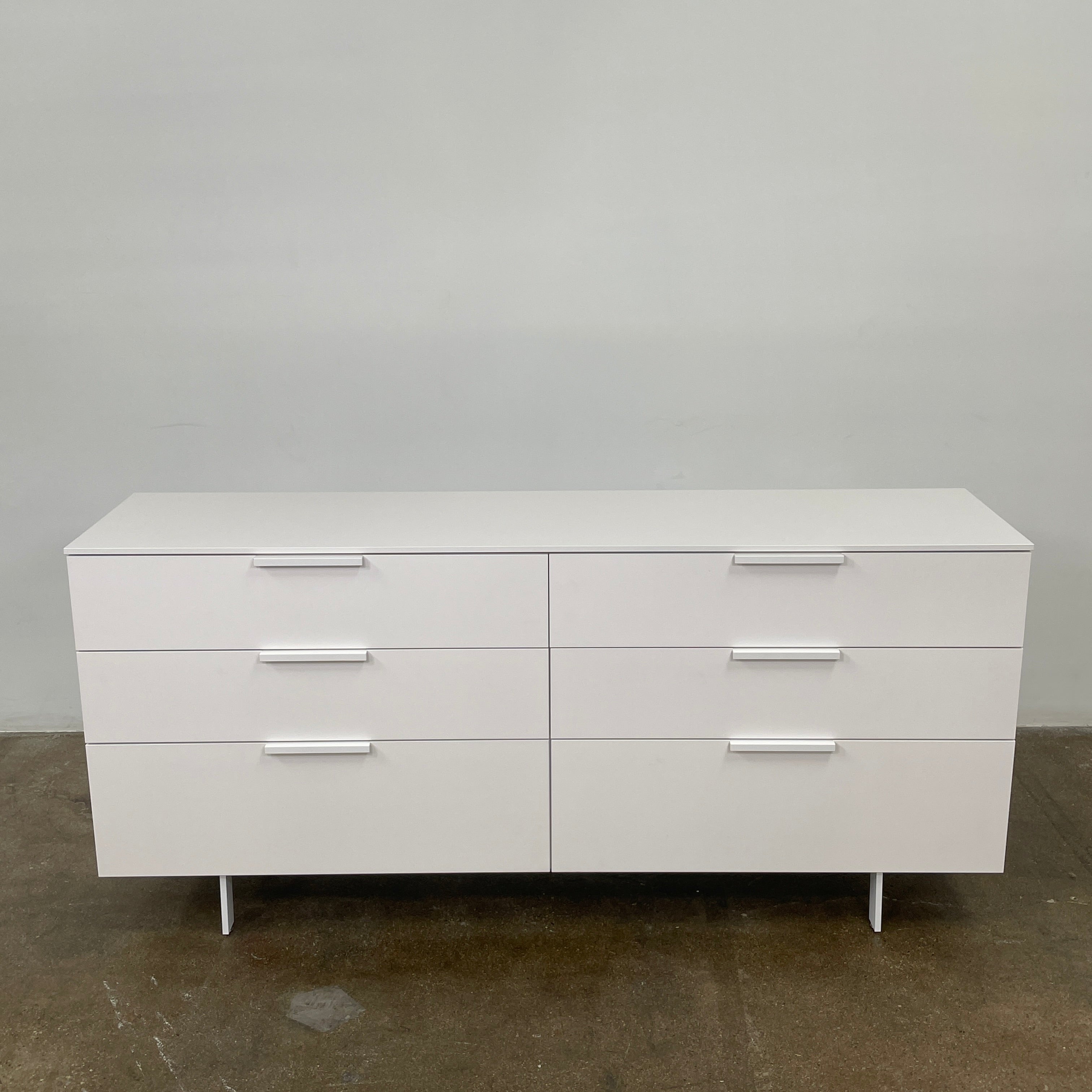 The Modern Resale Ligne Roset Everywhere 6 Drawer Dresser is a white, minimalist piece with sleek metal handles and two sturdy metal legs, elegantly presented in front of a plain white background.