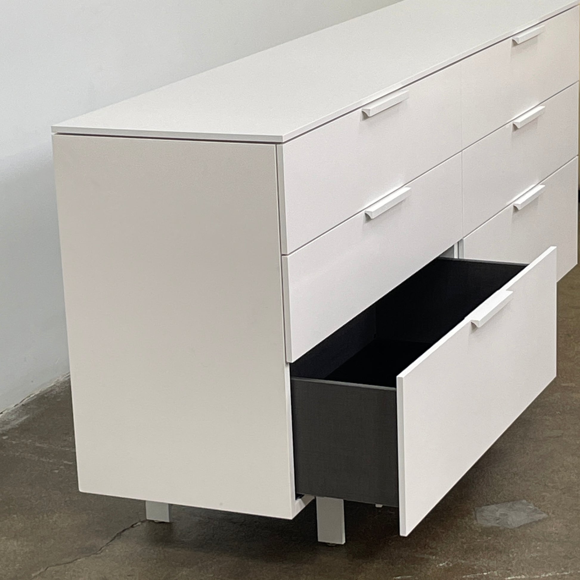 The Modern Resale Ligne Roset Everywhere 6 Drawer Dresser is a white, minimalist piece with sleek metal handles and two sturdy metal legs, elegantly presented in front of a plain white background.