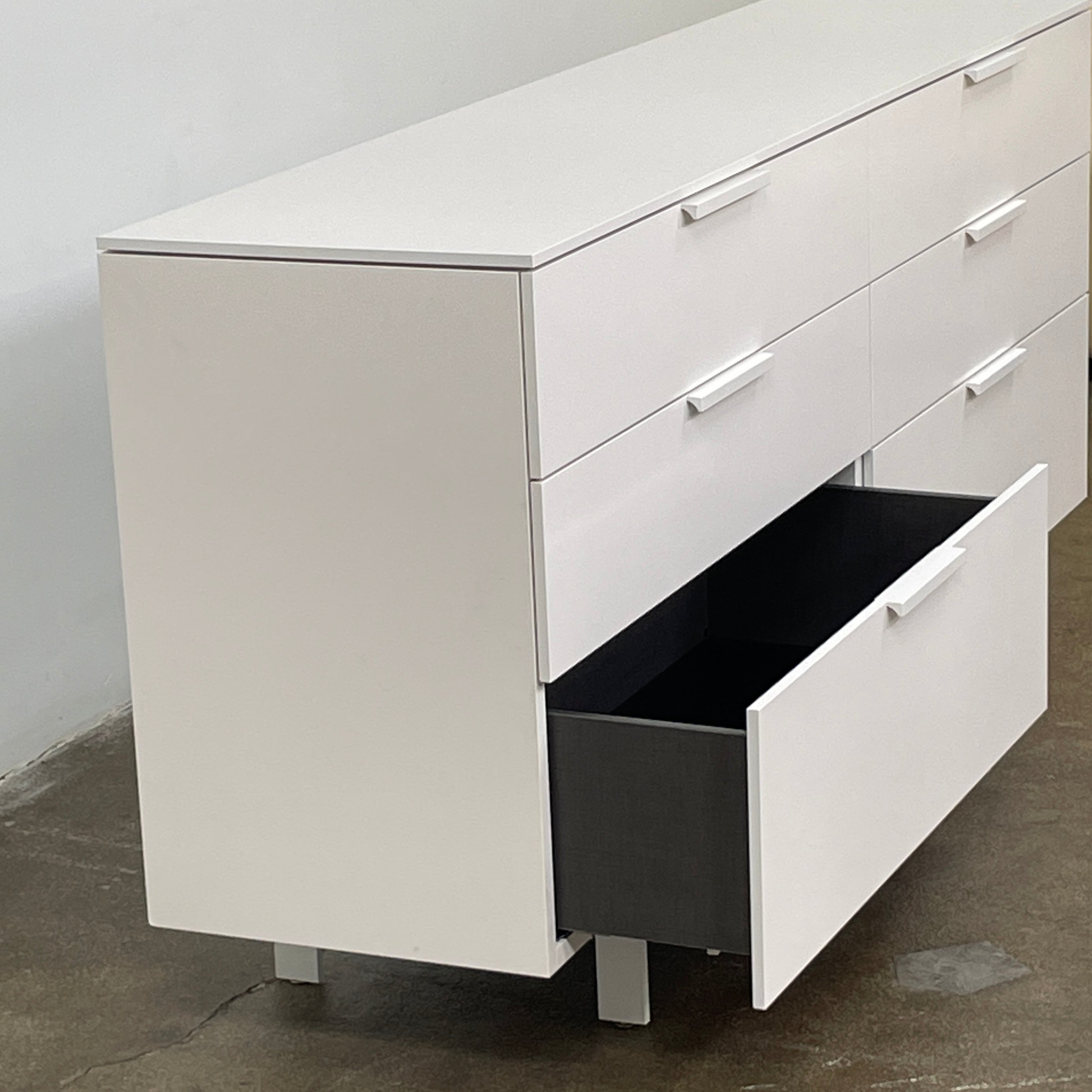 The Modern Resale Ligne Roset Everywhere 6 Drawer Dresser is a white, minimalist piece with sleek metal handles and two sturdy metal legs, elegantly presented in front of a plain white background.
