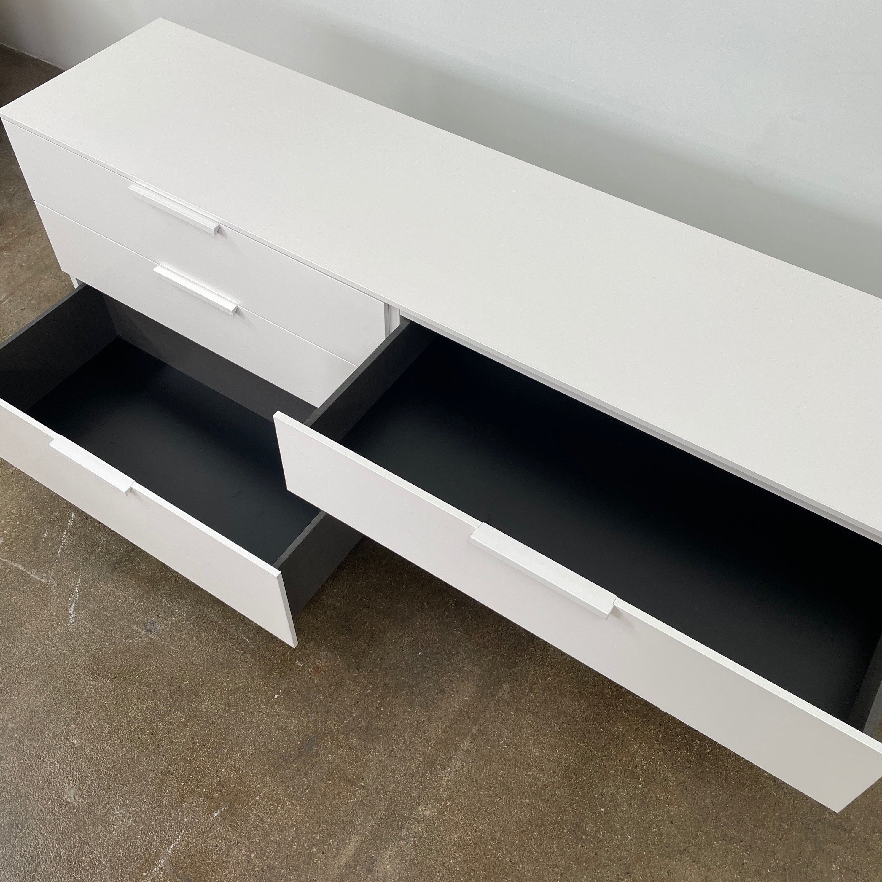 The Modern Resale Ligne Roset Everywhere 6 Drawer Dresser is a white, minimalist piece with sleek metal handles and two sturdy metal legs, elegantly presented in front of a plain white background.