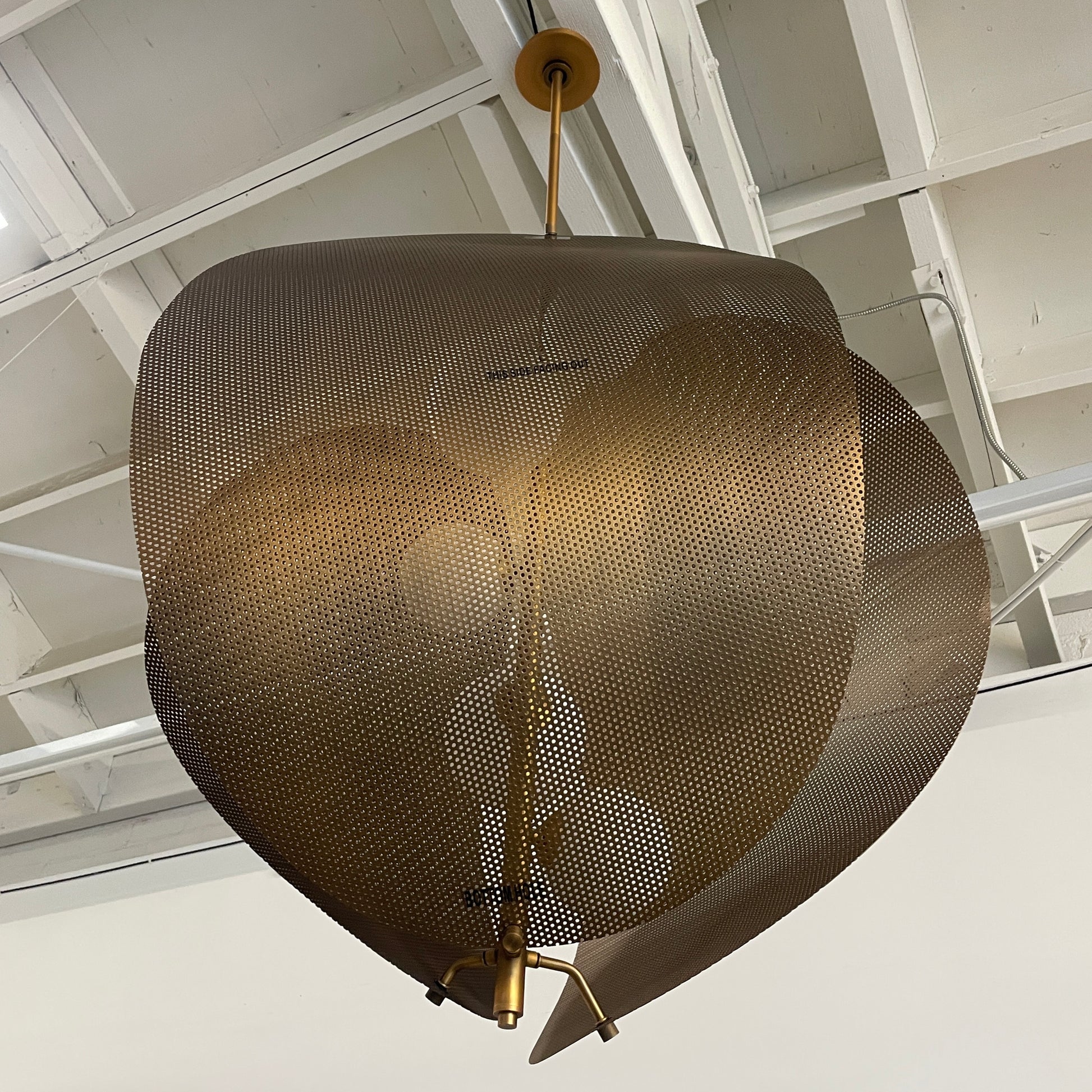 A modern chandelier with circular metal mesh panels and a central bulb hangs from a golden rod, reminiscent of the Studio M Chips 5-Light Vertical Pendant in Natural Aged Brass.