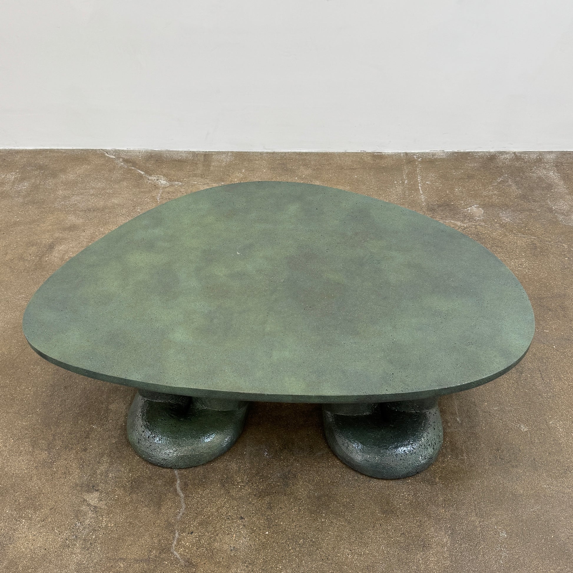 A low, irregularly shaped dark green Ian Felton Studio Mullunu Coffee Table with three thick, cylindrical legs stands on a plain white background.