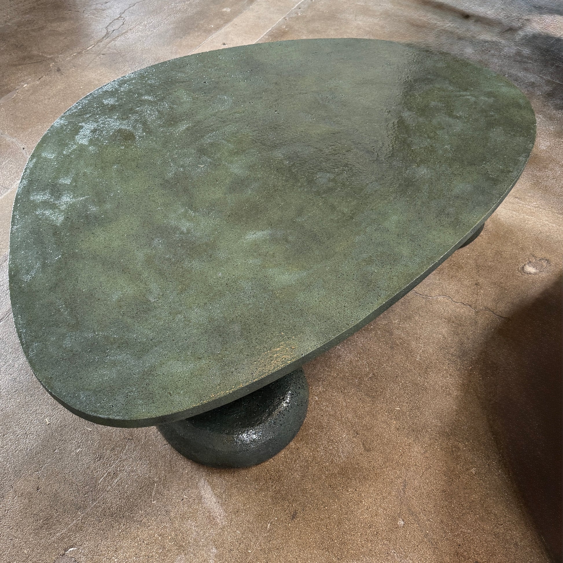 A low, irregularly shaped dark green Ian Felton Studio Mullunu Coffee Table with three thick, cylindrical legs stands on a plain white background.