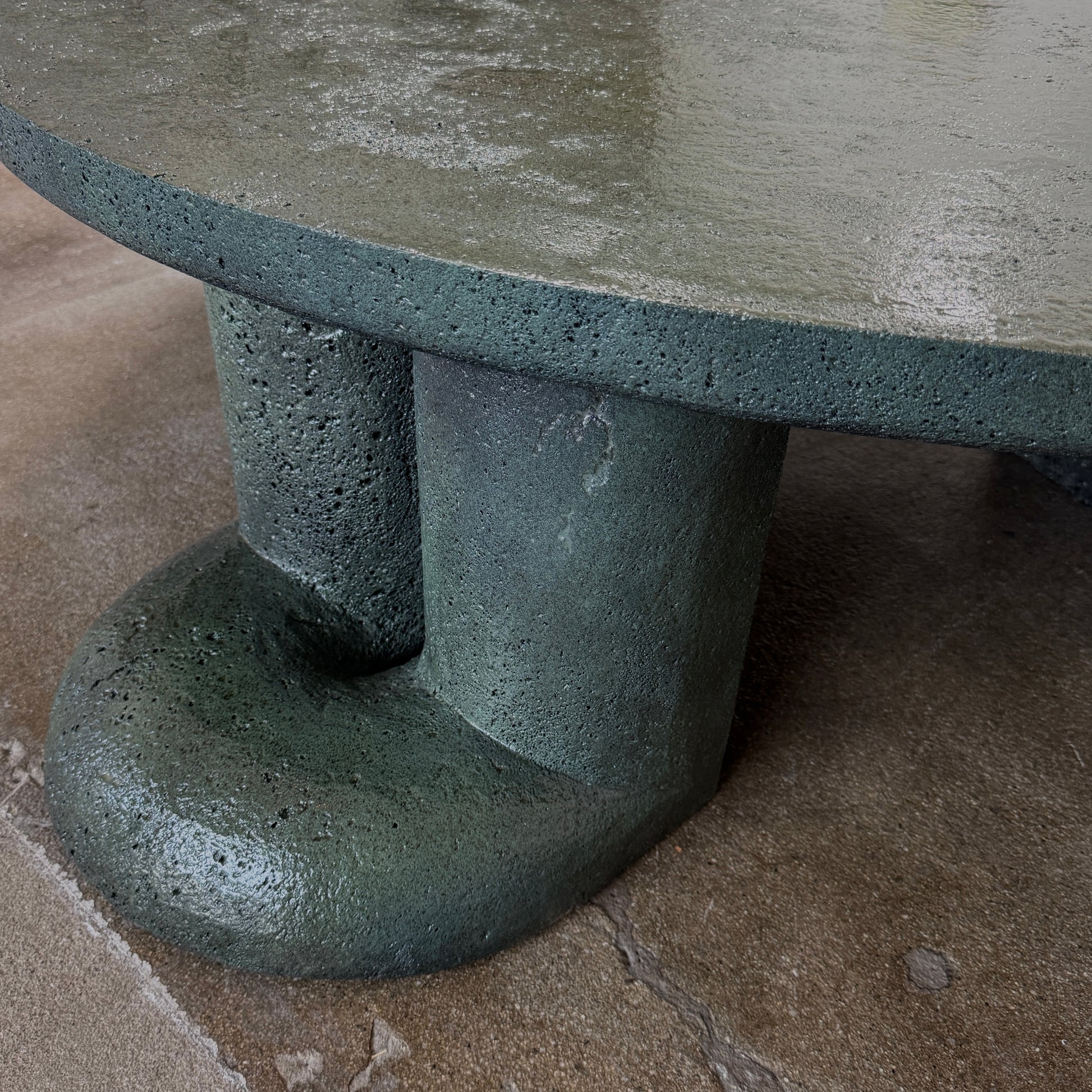 A low, irregularly shaped dark green Ian Felton Studio Mullunu Coffee Table with three thick, cylindrical legs stands on a plain white background.