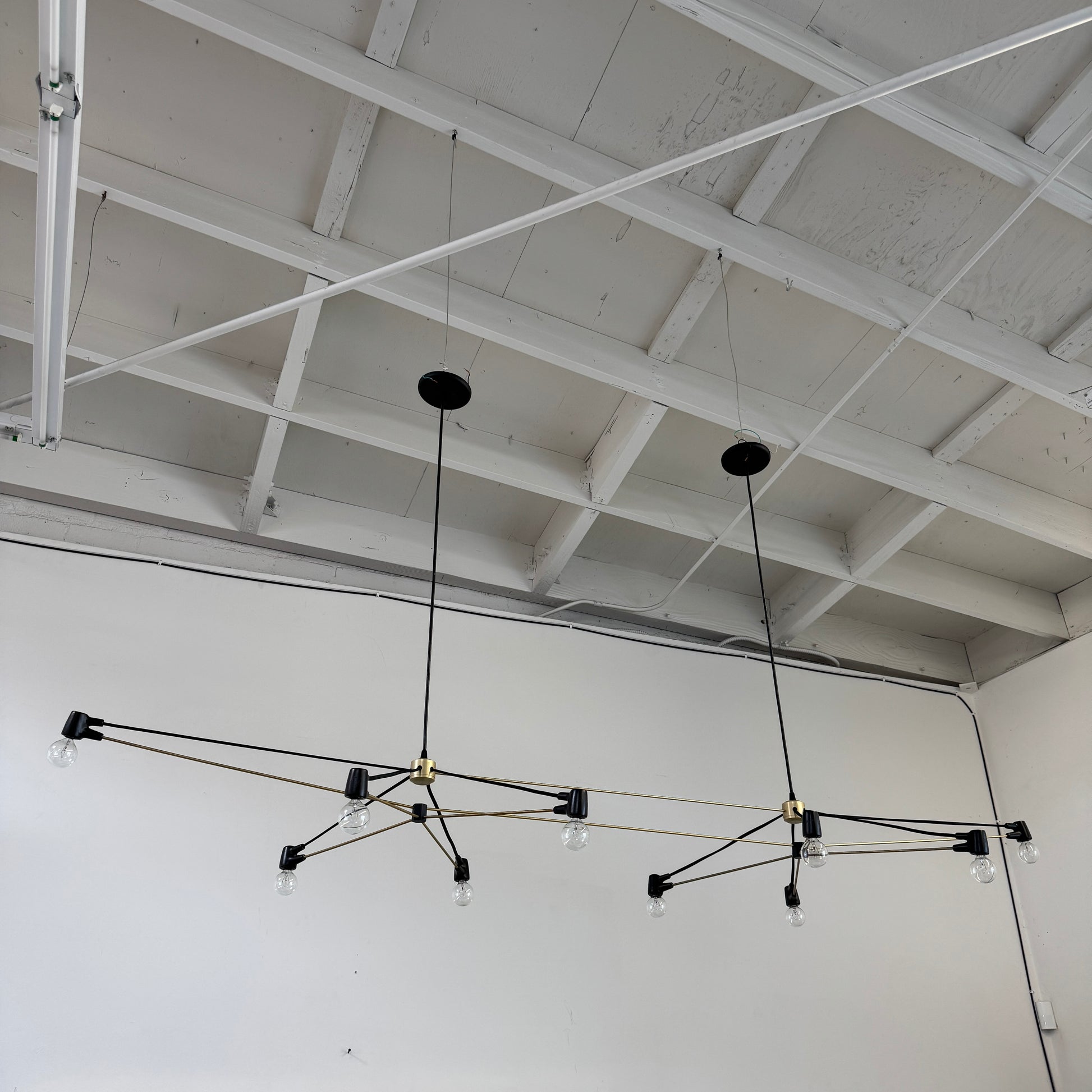 Two Ravenhill Studio Double Church Chandeliers by Ravenhill Studio, featuring exposed bulbs and modern black metal design, hang from a white industrial ceiling with visible beams, creating striking entryway lighting.