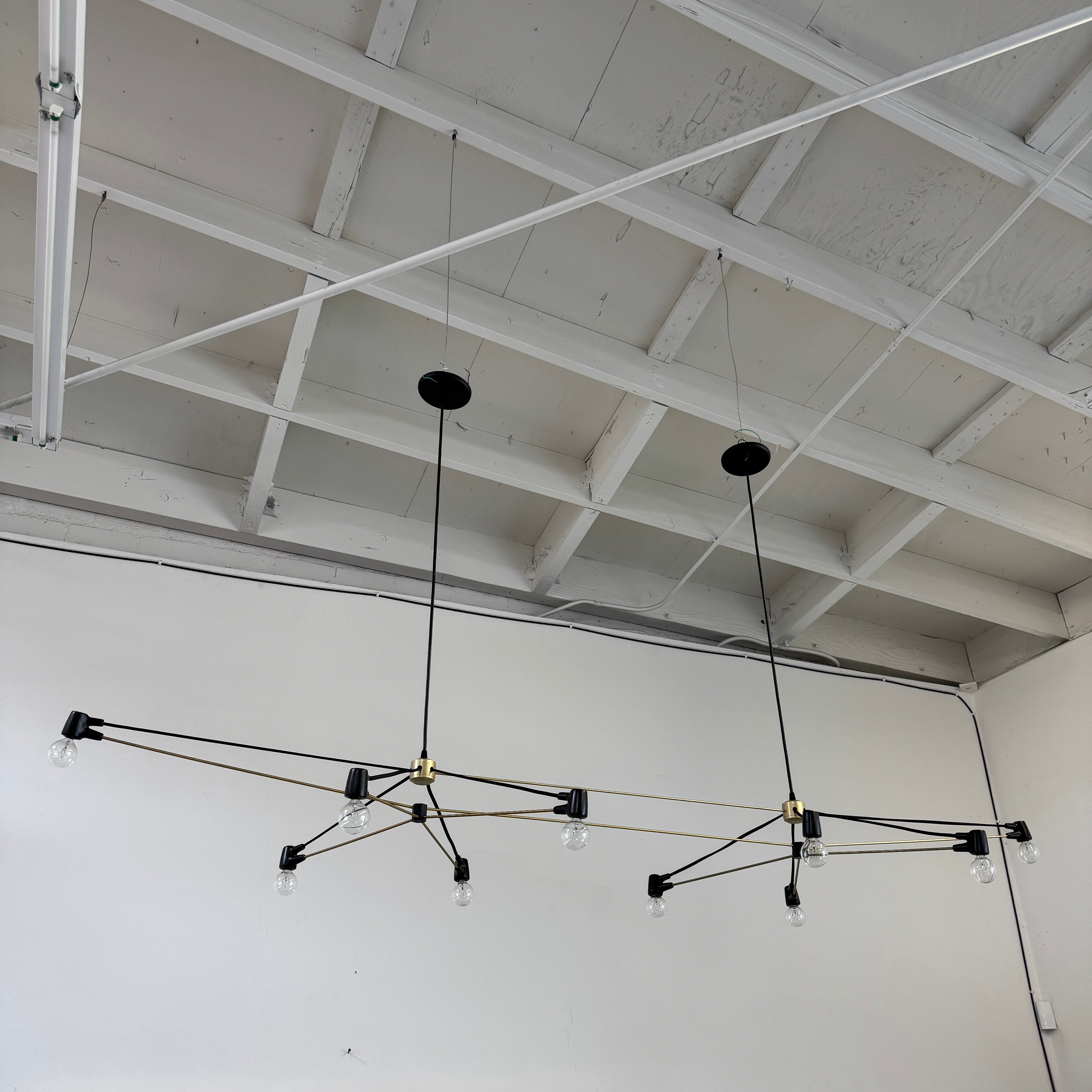 Two Ravenhill Studio Double Church Chandeliers by Ravenhill Studio, featuring exposed bulbs and modern black metal design, hang from a white industrial ceiling with visible beams, creating striking entryway lighting.
