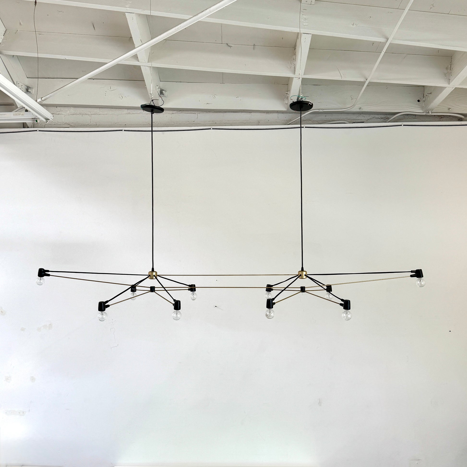 Two Ravenhill Studio Double Church Chandeliers by Ravenhill Studio, featuring exposed bulbs and modern black metal design, hang from a white industrial ceiling with visible beams, creating striking entryway lighting.