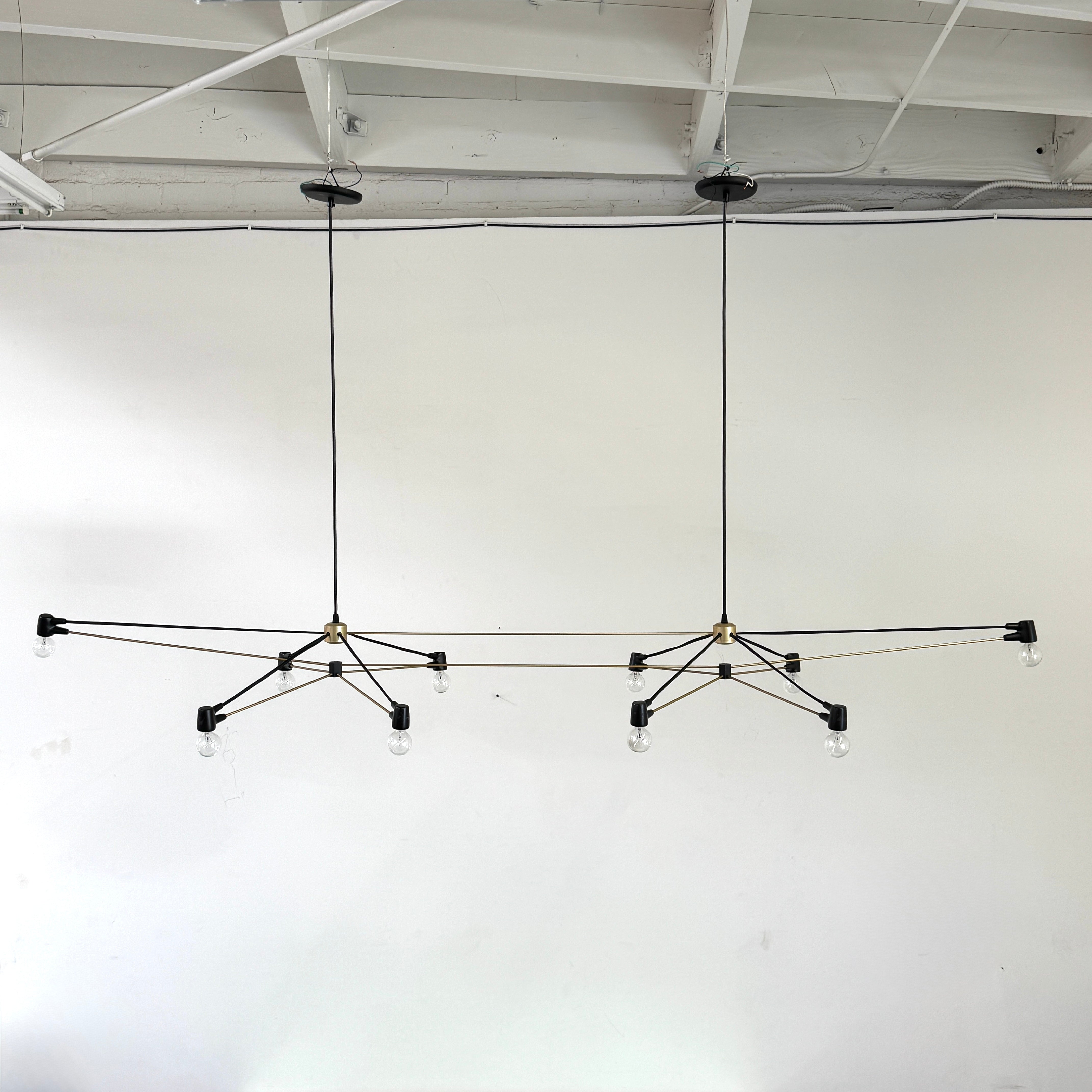 Two Ravenhill Studio Double Church Chandeliers by Ravenhill Studio, featuring exposed bulbs and modern black metal design, hang from a white industrial ceiling with visible beams, creating striking entryway lighting.